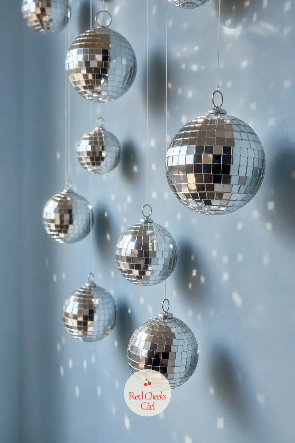 A Cascade of Mirrored Disco-Ball Ornaments Hung at Staggered Heights Down a Blank Wall — This is the idea for anyone who wants sparkle without buying a single
