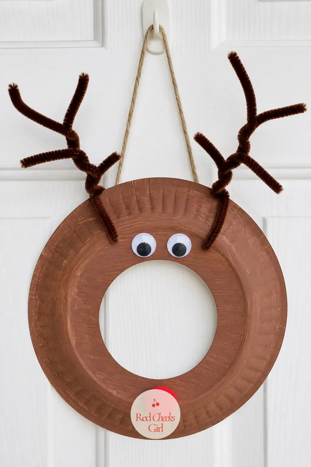 Rudolph Paper Plate Wreath — A brown-painted paper plate ring becomes Rudolph with two googly eyes, a round red pom nose glued dead center at the bottom, and a