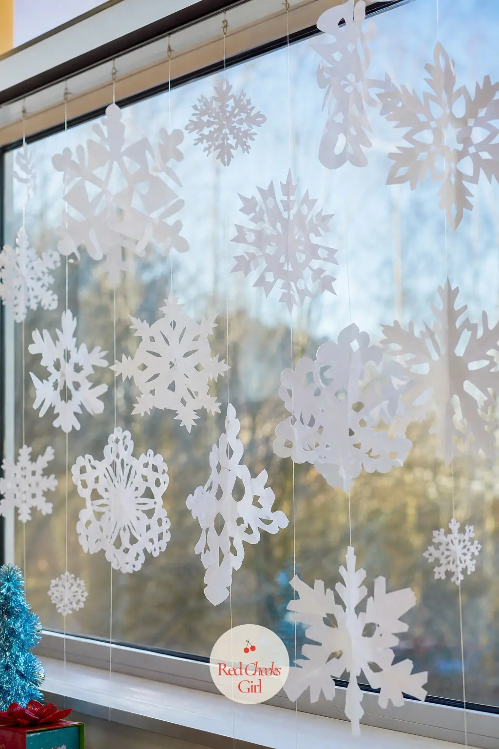 A Cut Paper Snowflake Curtain Hung From the Window Rail — Fold and cut white cardstock snowflakes in three or four sizes, then suspend them from fishing line