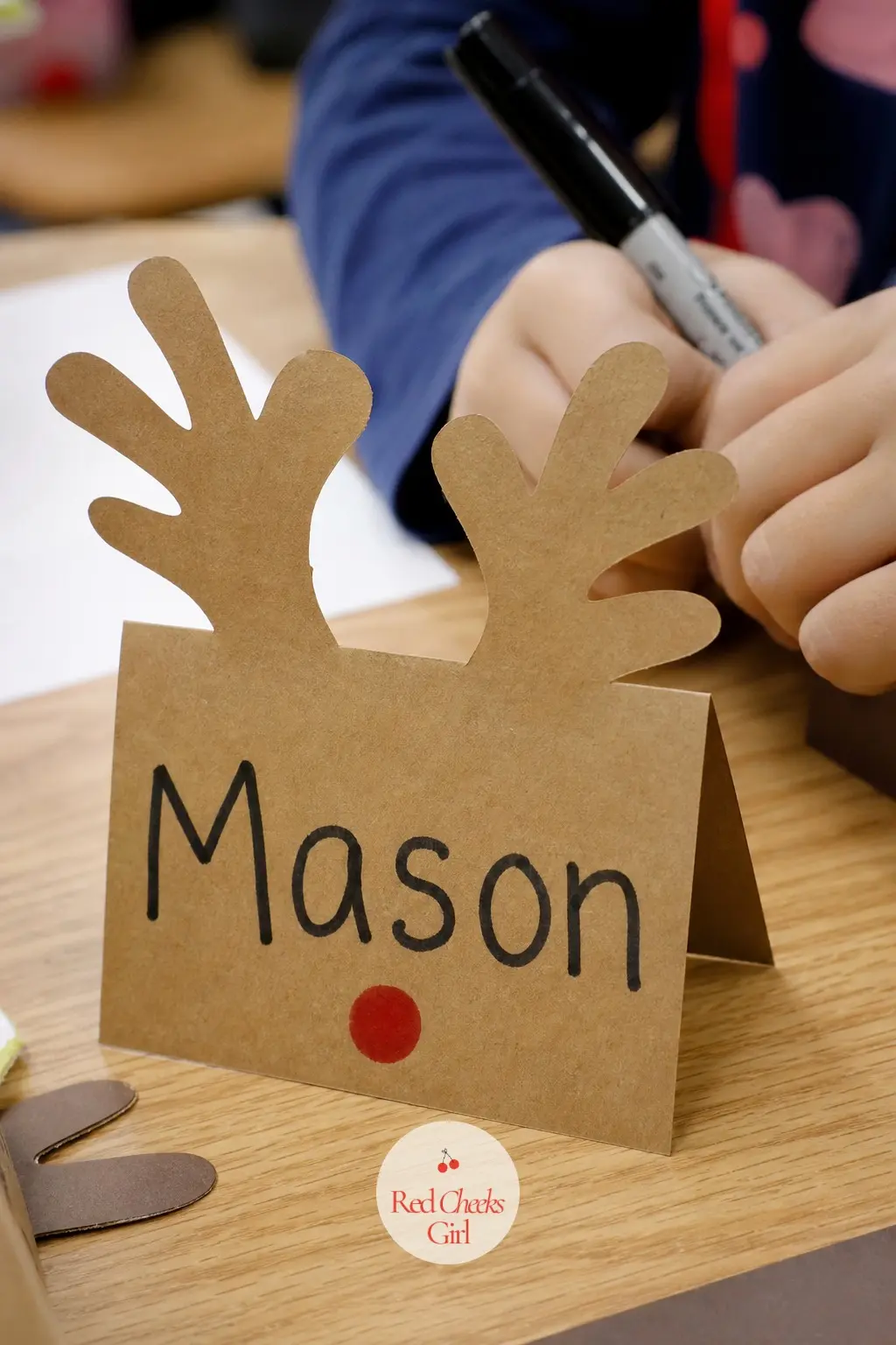 A Paper Reindeer Antler Name Plate Standing on Each Desk — Fold a simple tent card from brown cardstock, punch a pair of antler shapes into the top edge, and