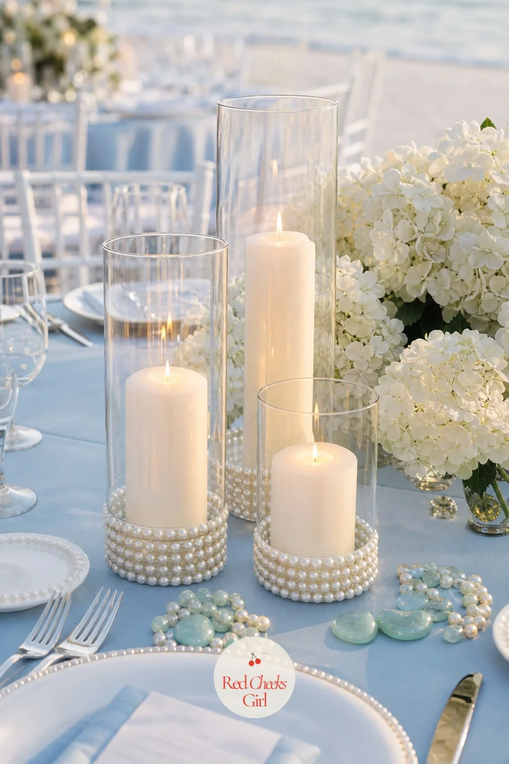 A Candle Cluster in Pearl-Trimmed Hurricanes — Once the sun drops, flowers stop doing the work and light takes over, and a single tall candle per table reads