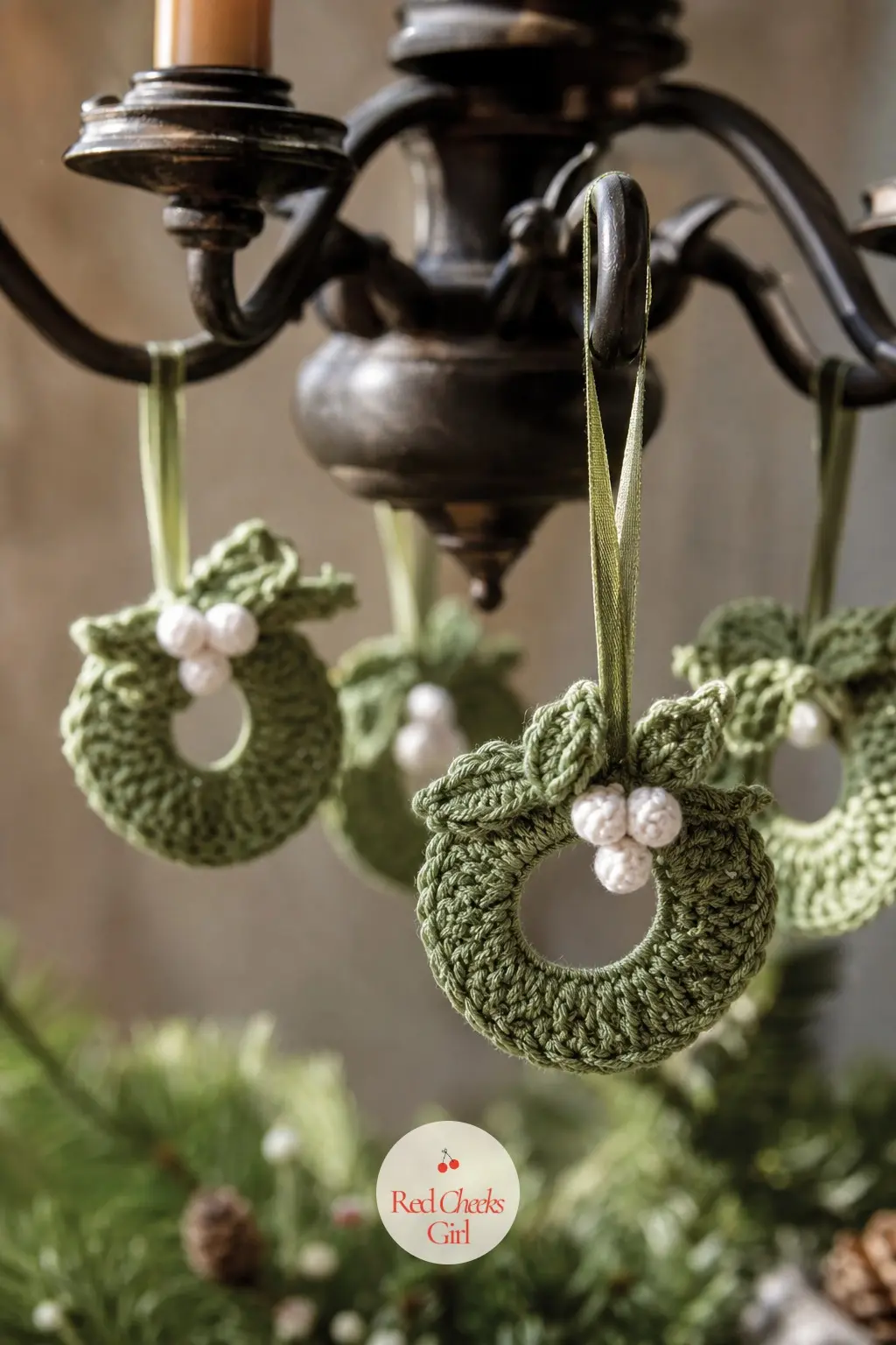 The Mini Mistletoe Crochet Wreaths for the Chandelier — Palm-sized rings in sage green with a few crocheted white mistletoe berries hang from ribbon loops off