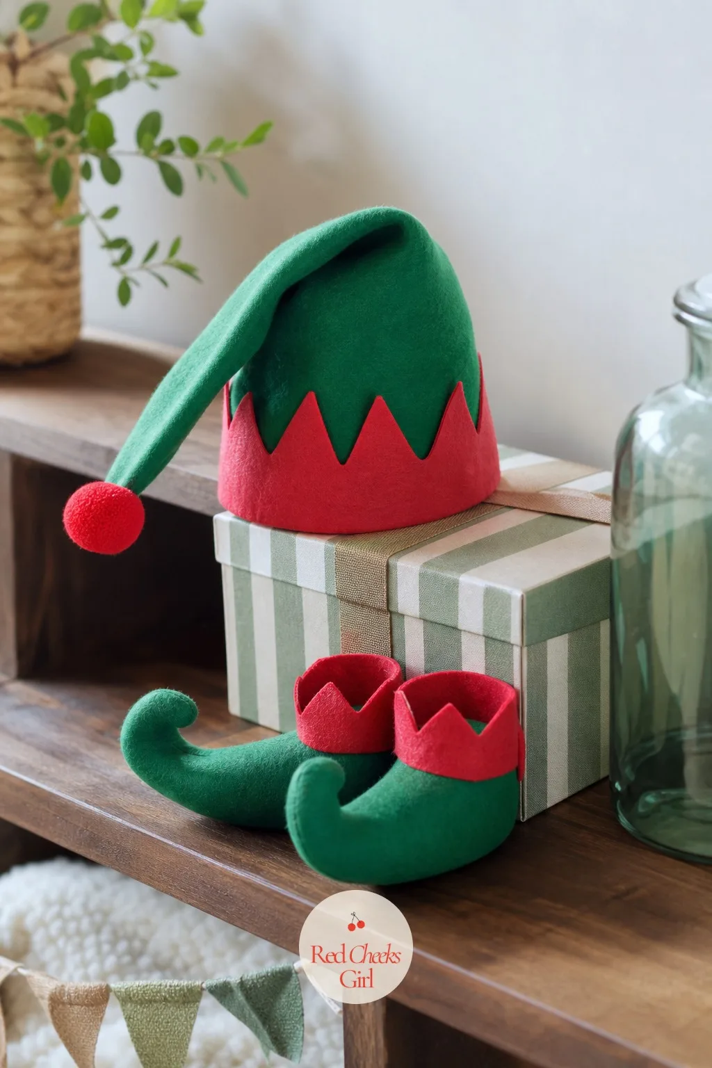 Little Elf — Green and red here stay playful rather than formal: a felt elf hat sits propped against a small gift box, striped candy-colored ribbon trails from