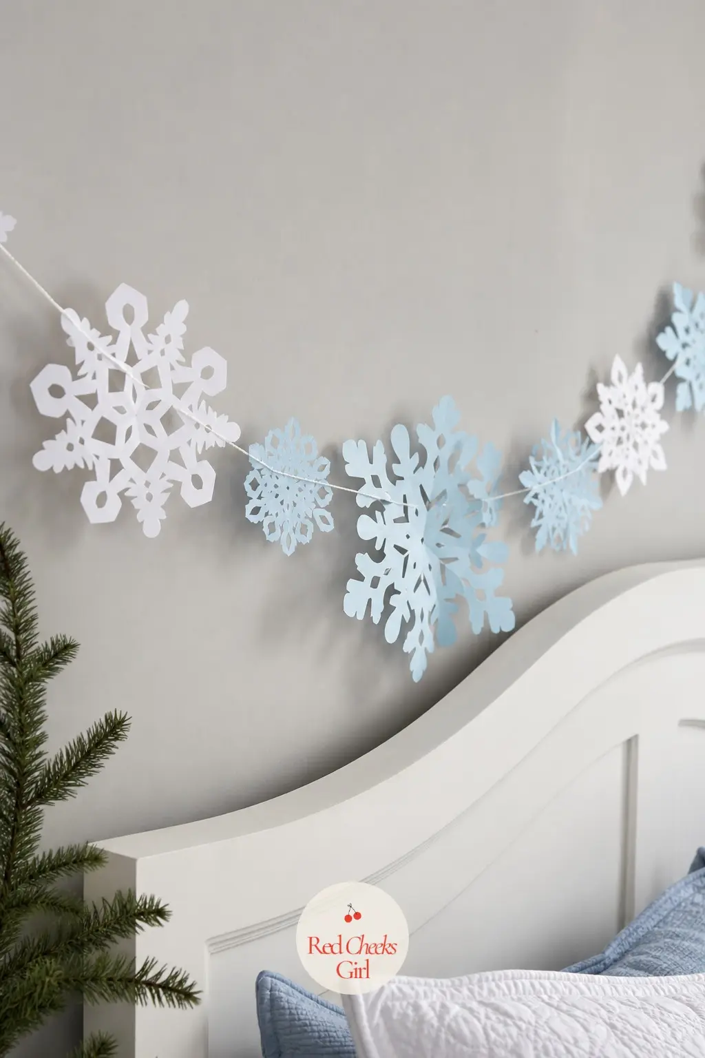 Paper Snowflake Garland — Folded and cut paper snowflakes in white and pale blue, strung at varying heights, give a bedroom wall a soft winter look without a