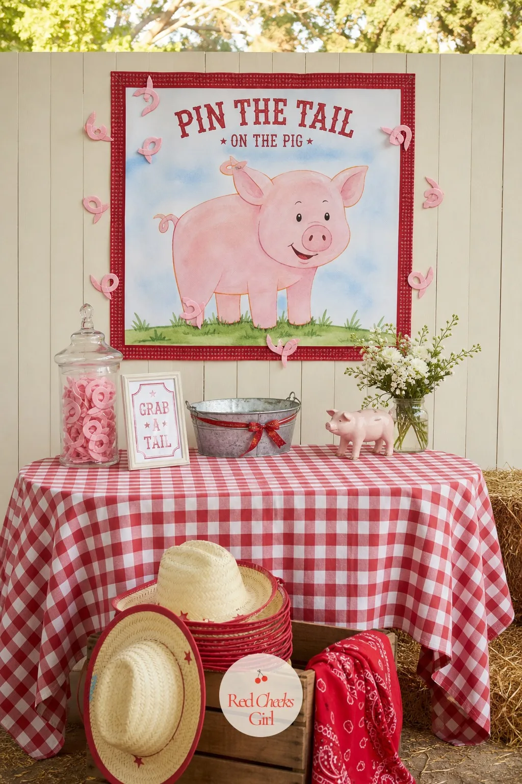 Pin the Tail on the Pig Corner — A large pink pig poster hangs flat against a cream fence board or garden wall, a scatter of small felt tails already pinned at