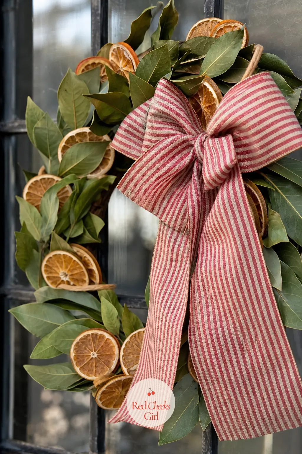 The Ticking Stripe Bow and Dried Orange Wreath for the Greenhouse Door — A brick-red ticking stripe bow sits against dried orange slices and a few bay leaf