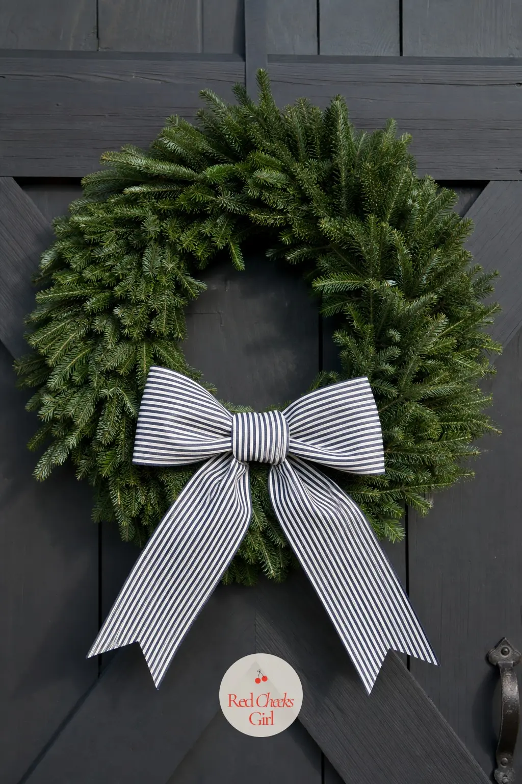 The Ticking Stripe Bow and Fir Wreath for the Carriage House Door — A wide navy and white ticking stripe bow sits low on a full fir wreath, the stripe doing