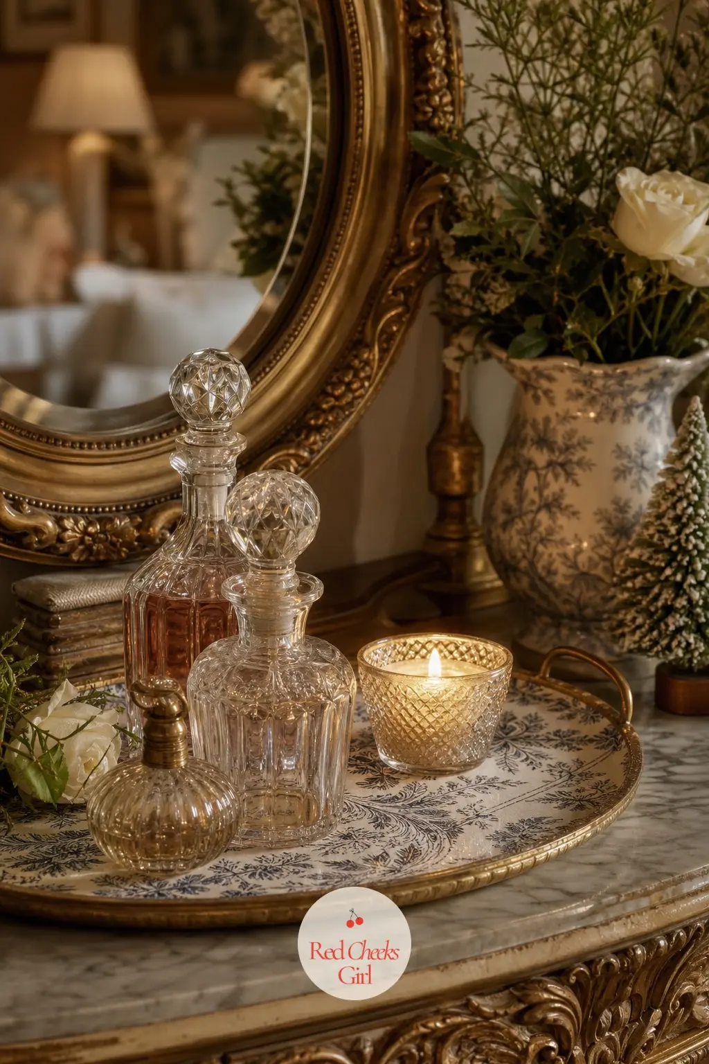 The Dressing Table, Lit for the Evening — A small vanity holds a round mirror, two glass perfume bottles, and one low candle, with a toile-print tray