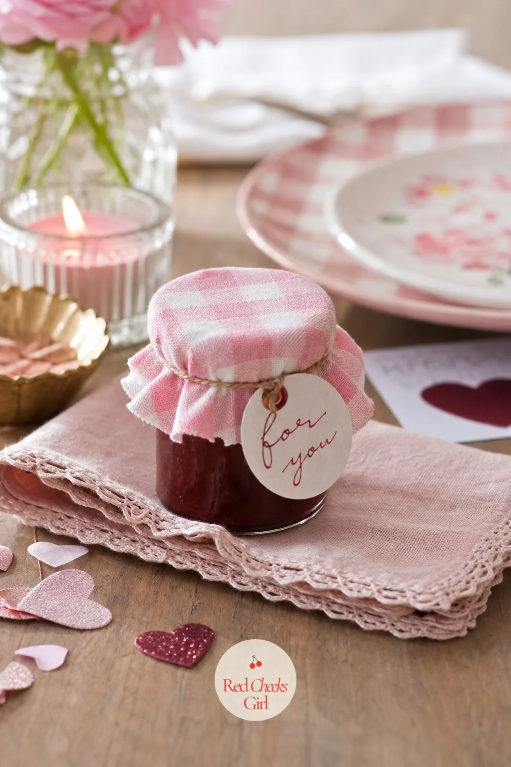 The Tiny Jar of Strawberry Jam with a Gingham Lid — A small glass jar of strawberry jam, lid covered in pink gingham fabric and held on with a rubber band