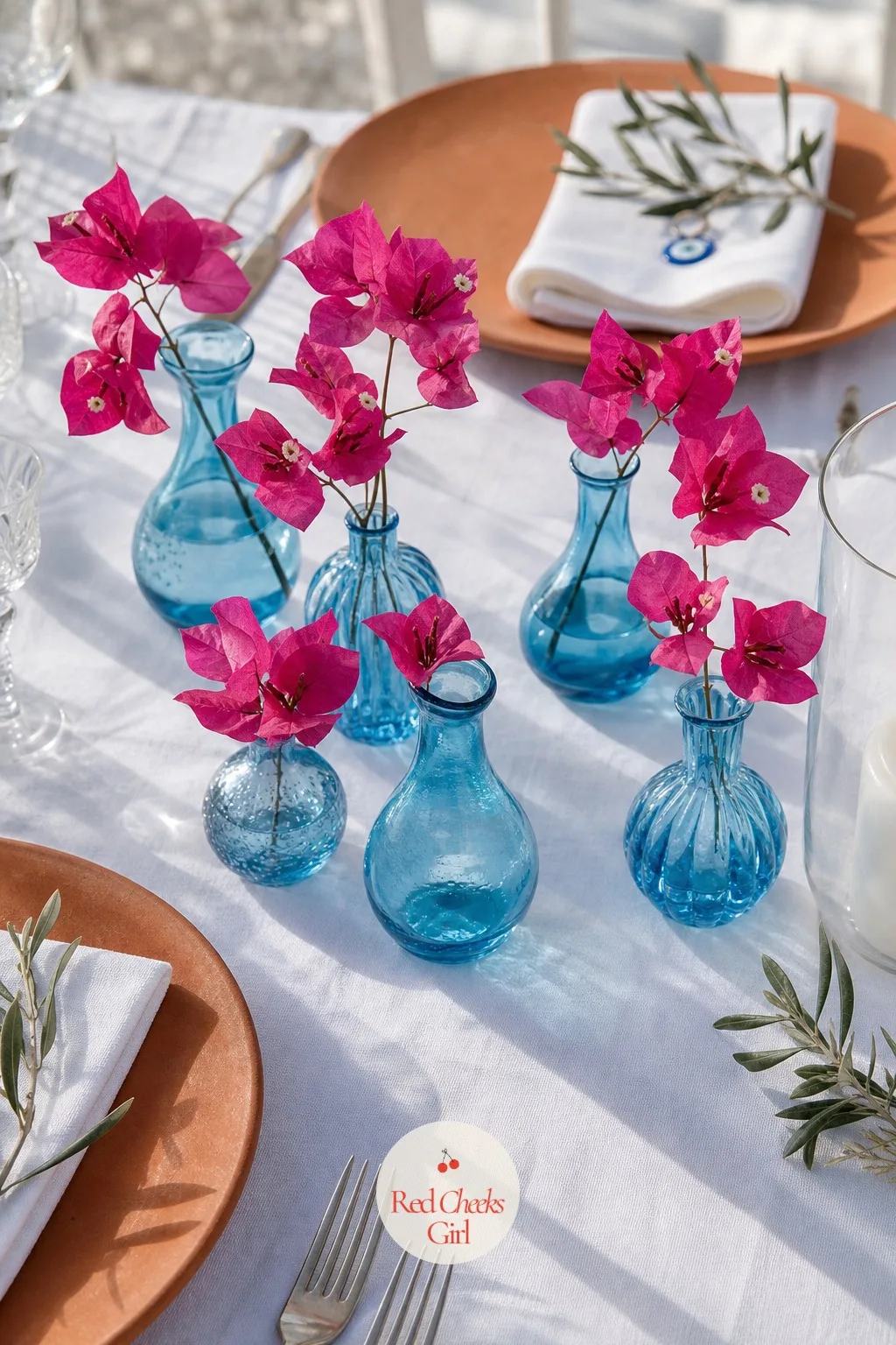 Bougainvillea Bud Vases — Between the place settings, a scattering of small blue glass vases keeps the colour alive right at eye level, where the big arch and