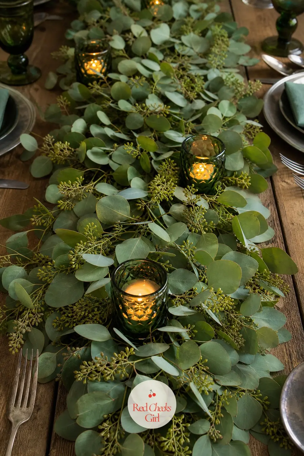 The Table Runner, Laid in Fresh Eucalyptus and Emerald Glass — A runner of fresh eucalyptus down the centre of the table, studded with emerald glass votives