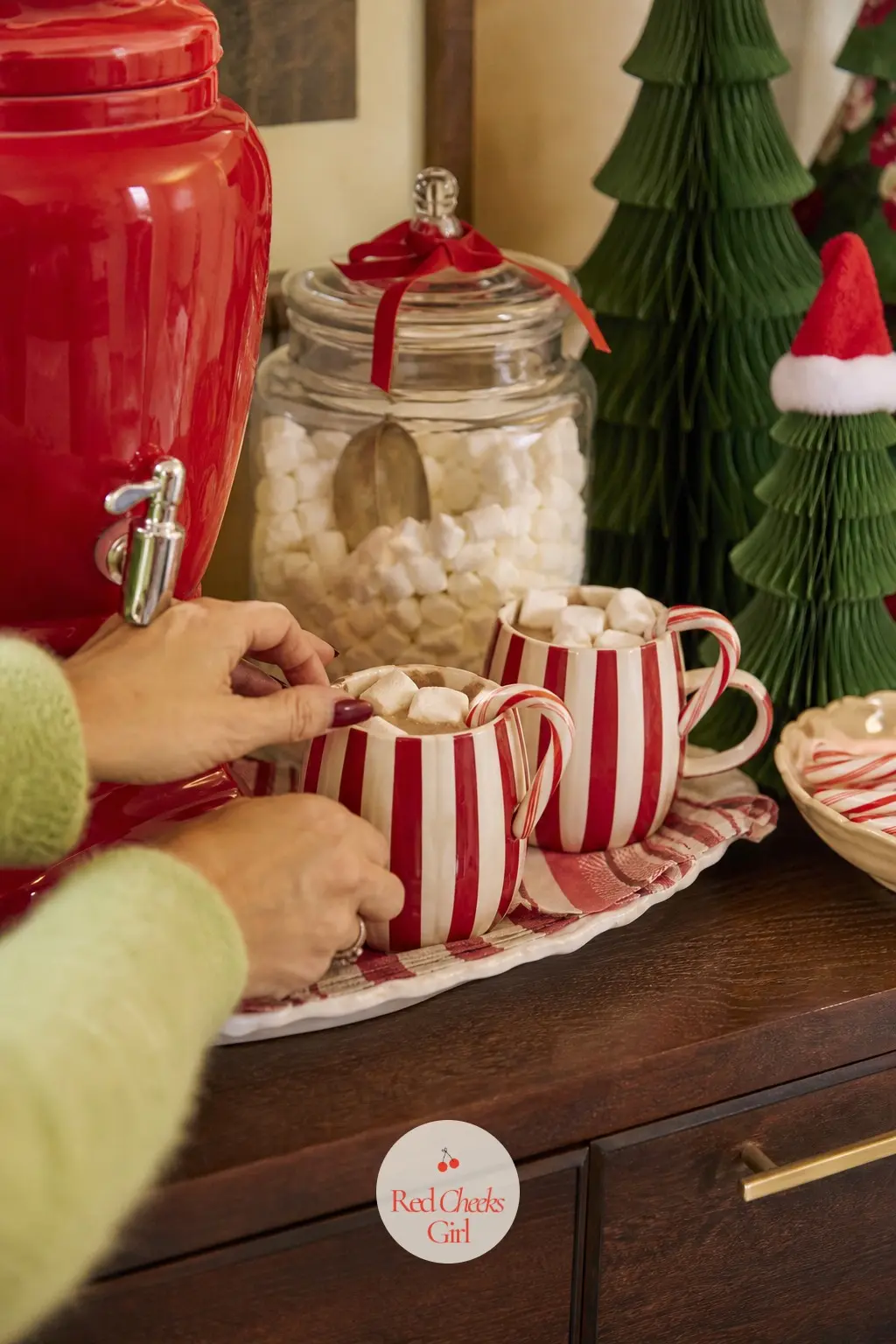 A Crooked Cocoa Bar on the Sideboard — A small bar cart or sideboard corner set up with striped mugs, a cherry red drink dispenser and a jar of marshmallows