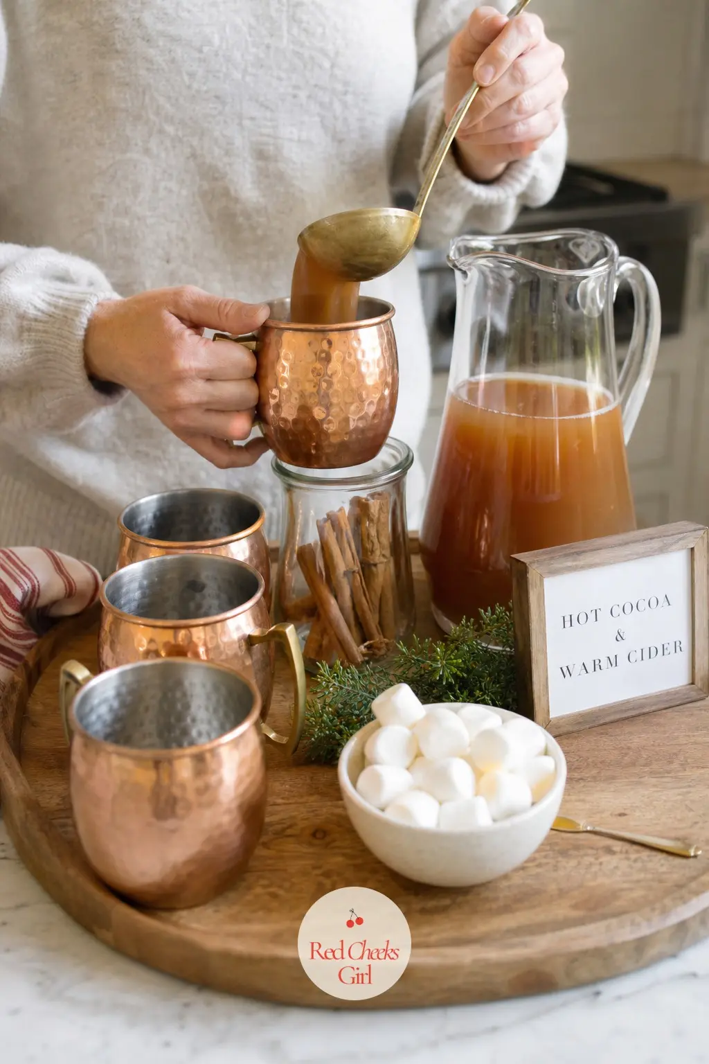 A Hot Cocoa and Cider Station on the Counter — A tray of polished copper mugs, a jar of cinnamon sticks, a small pitcher of amber cider and a bowl of cream