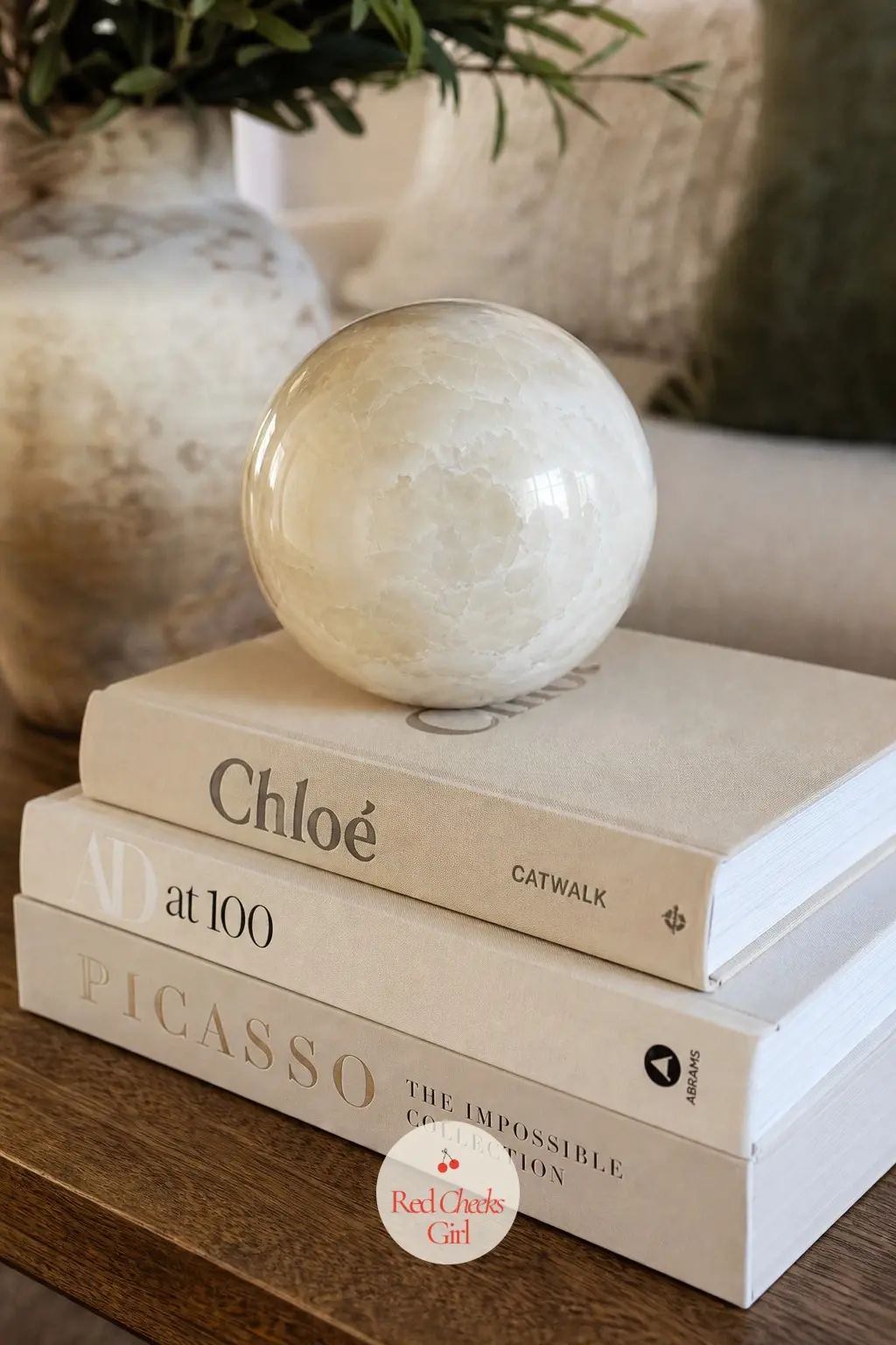 A Stack of Art Books Topped with an Alabaster Orb on the Coffee Table — Three cream-covered books, stacked tallest to shortest, with a single pale alabaster