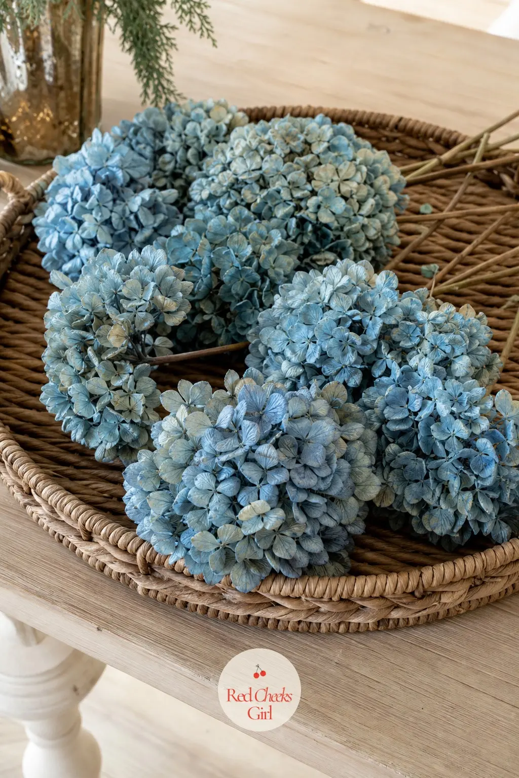 A Woven Tray of Blue Hydrangea Stems on the Side Table — Dried blue hydrangea heads, laid flat across a woven rattan tray rather than stood up in a vase, give