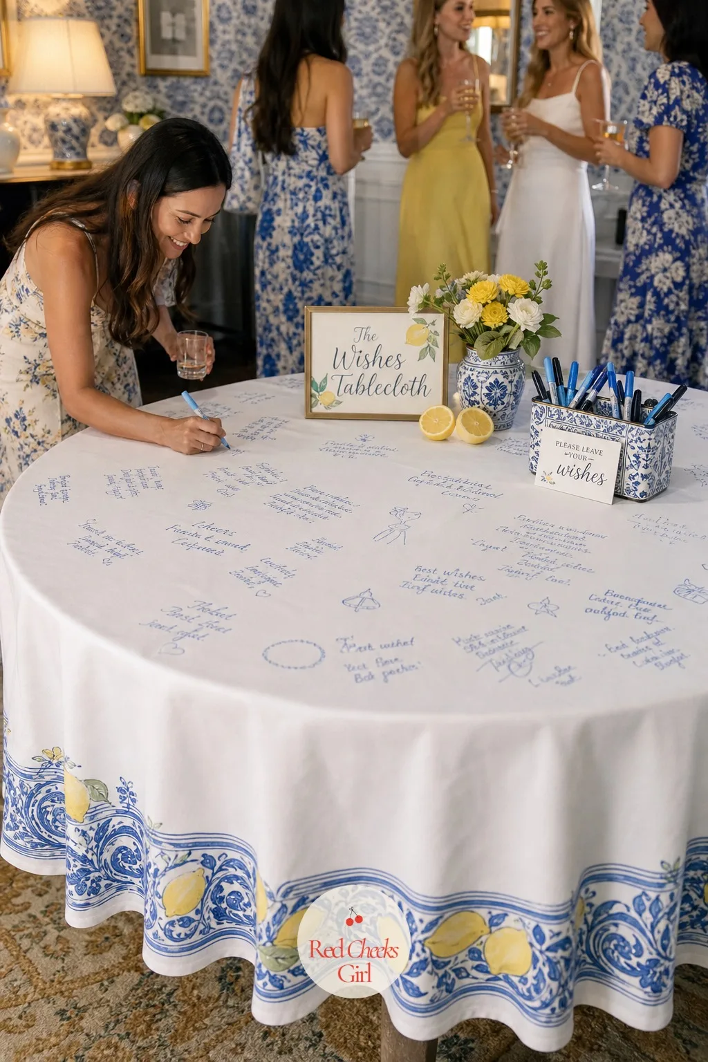 The Wishes Tablecloth Guests Sign and Draw On — A plain white cotton tablecloth, printed lightly with a lemon and tile border so it already feels dressed, lies