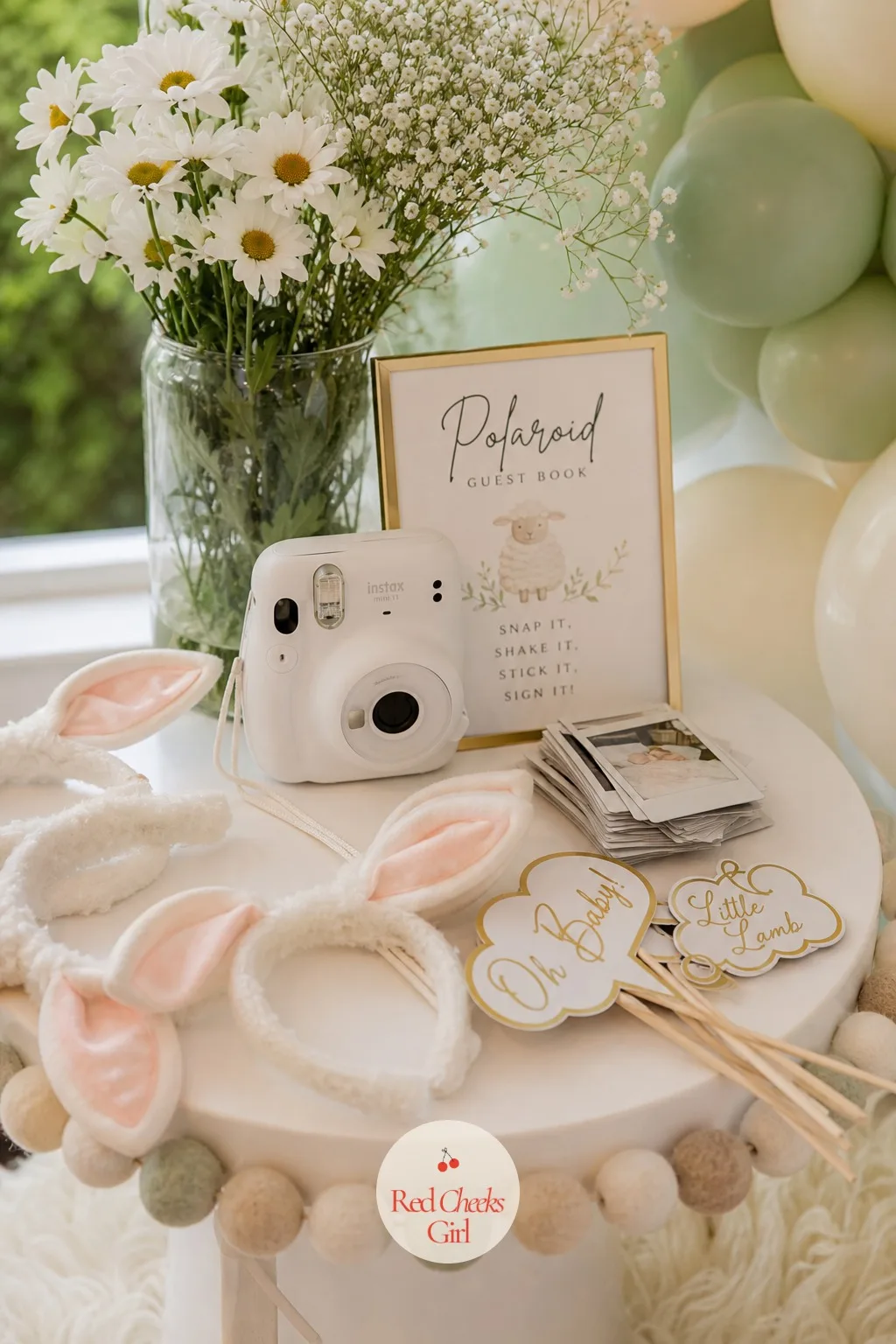 Polaroid Prop Table — A small side table holds a basket of soft felt lamb ear headbands, a few gold cardboard speech bubble props and an instant camera with a
