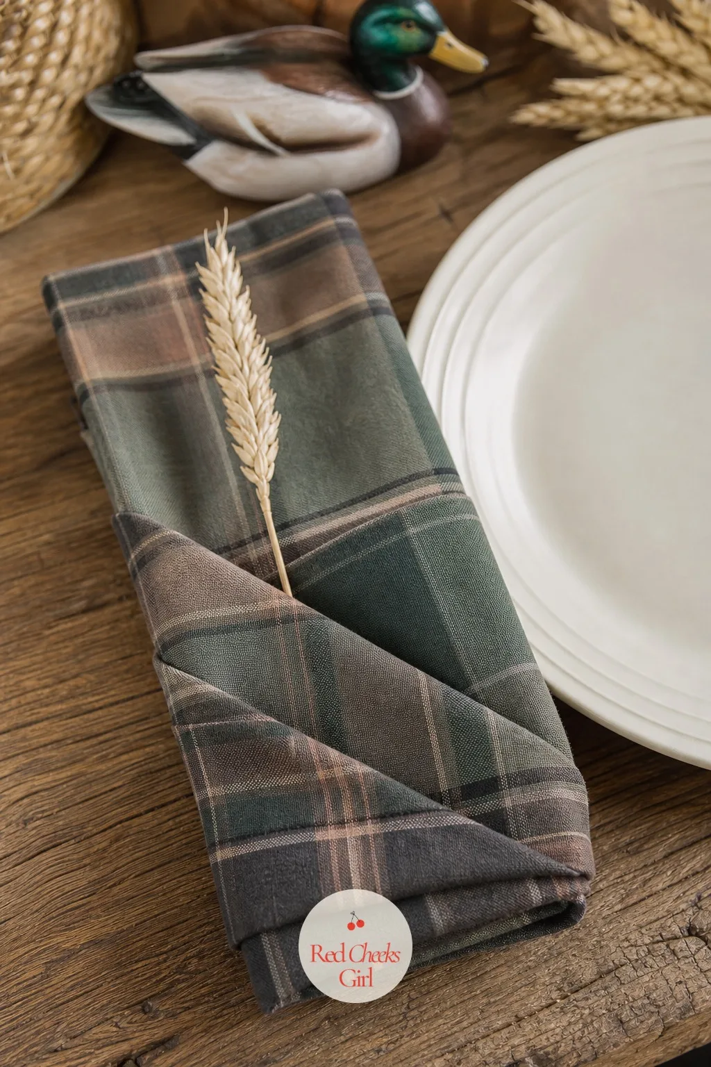Folded Plaid Napkin with a Wheat Sprig — The small detail at each place setting is the one guests actually touch, so it is worth the extra two minutes per