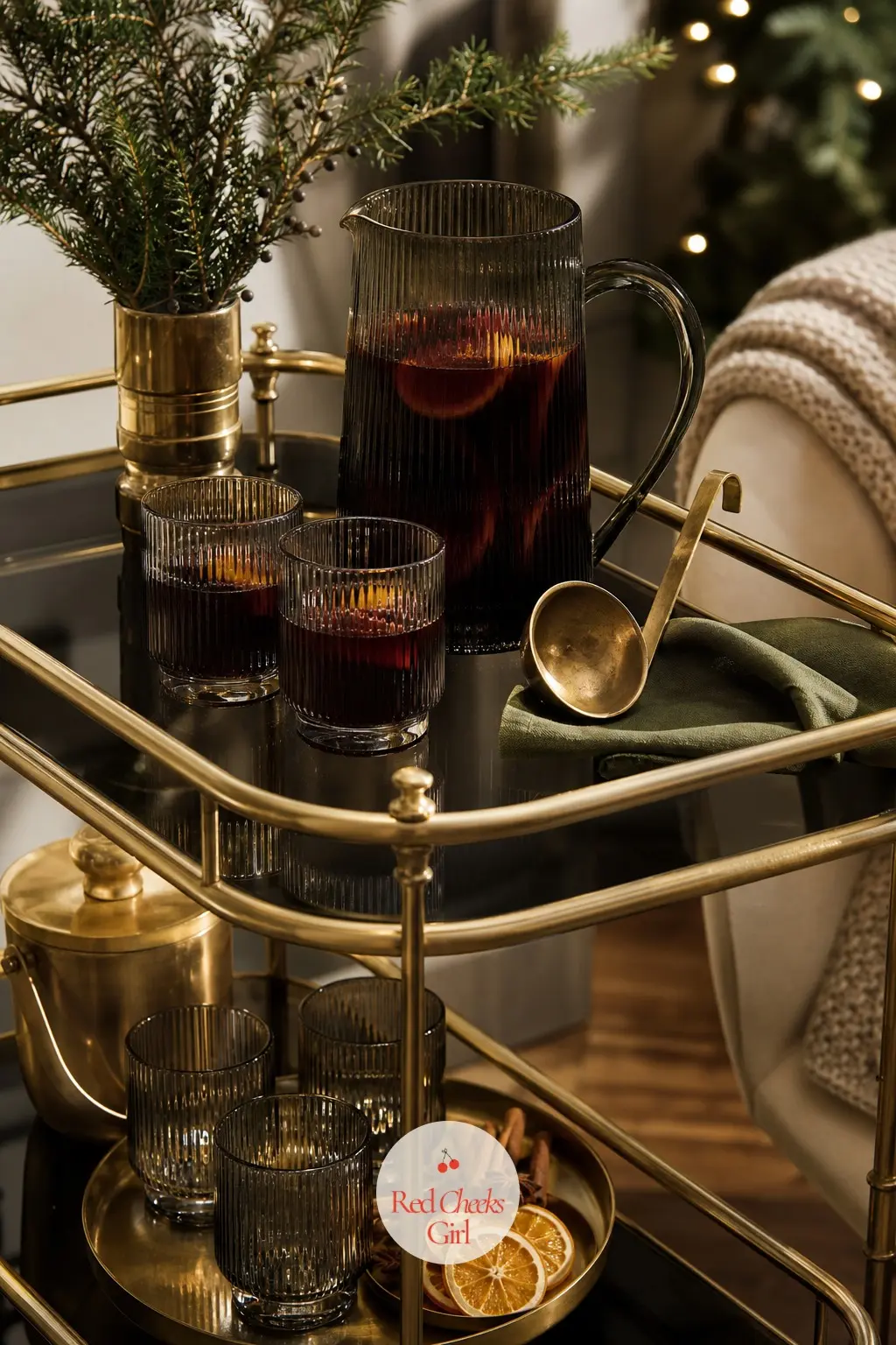 A Bar Cart Styled For Mulled Wine In Smoked Glass And Brass — A brass and smoked glass bar cart holds the evening drinks station: a set of smoked tumblers, a