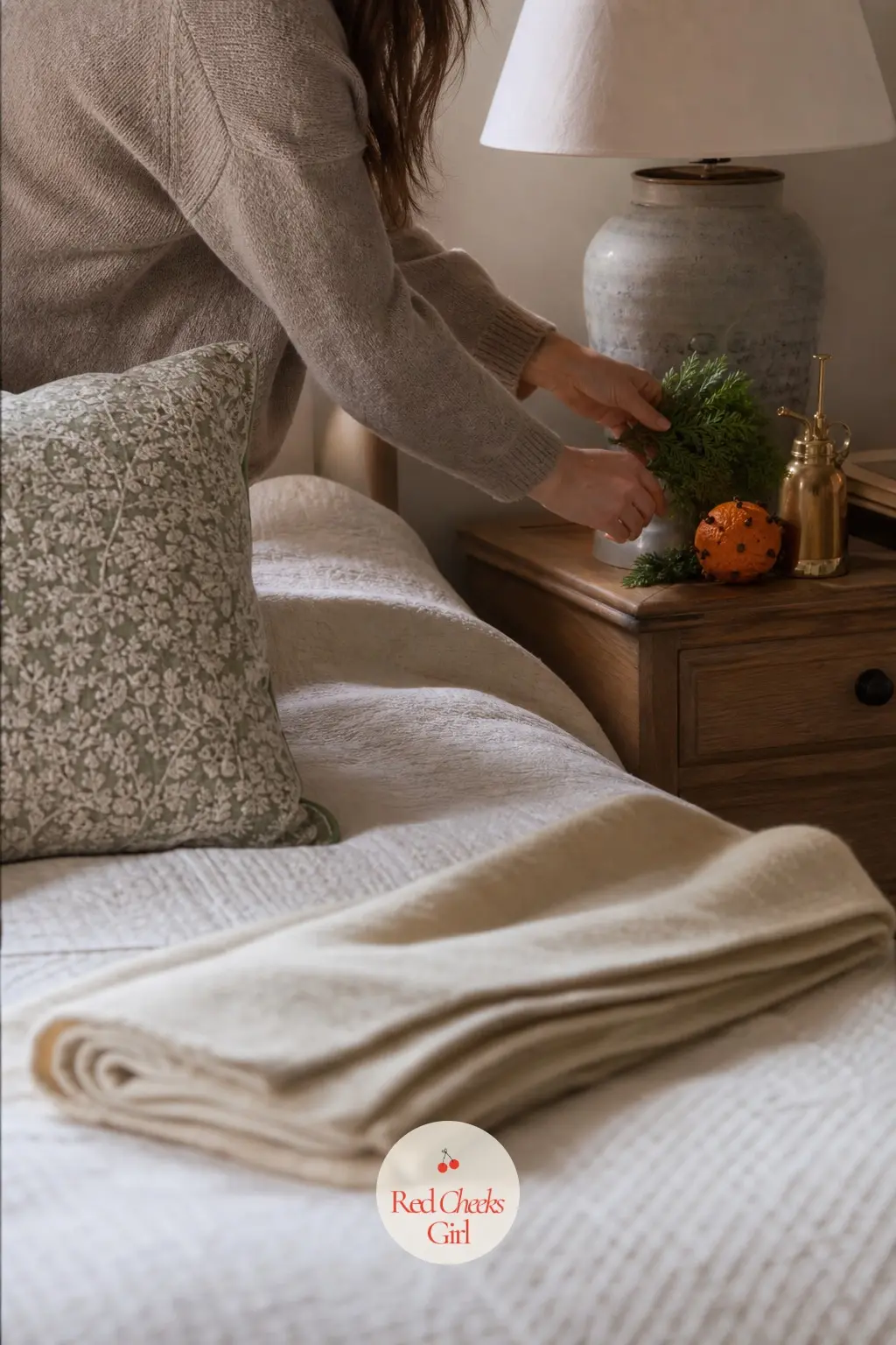 A Guest Room That Feels Thought Through — A cream knit throw folded at the foot of the bed, a small dried orange pomander and a sprig of fresh greenery on the