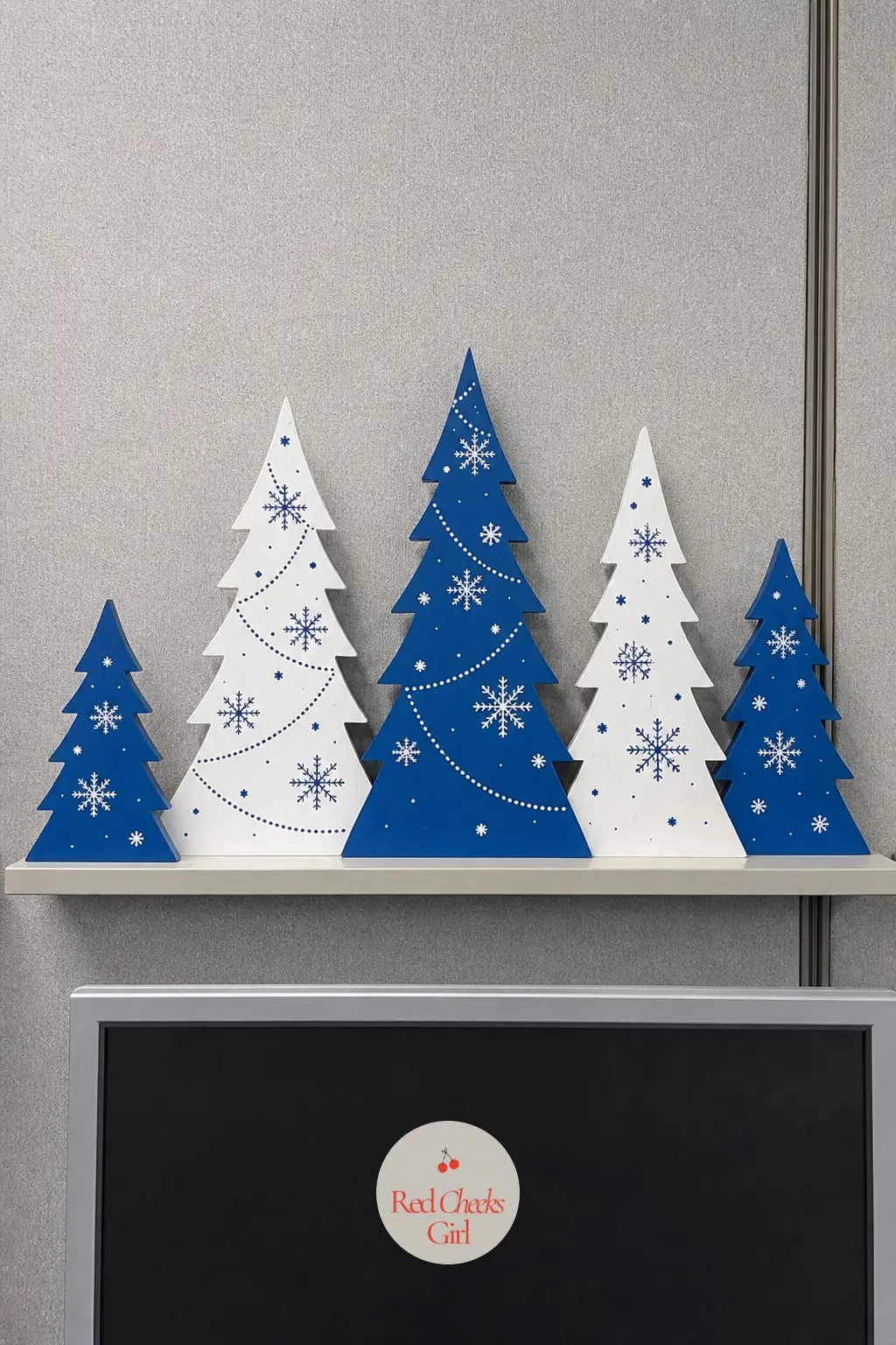 A Monitor-Top Shelf Holding a Row of Painted Wooden Trees — A slim shelf that clips above a monitor turns otherwise wasted vertical space into a tiny display