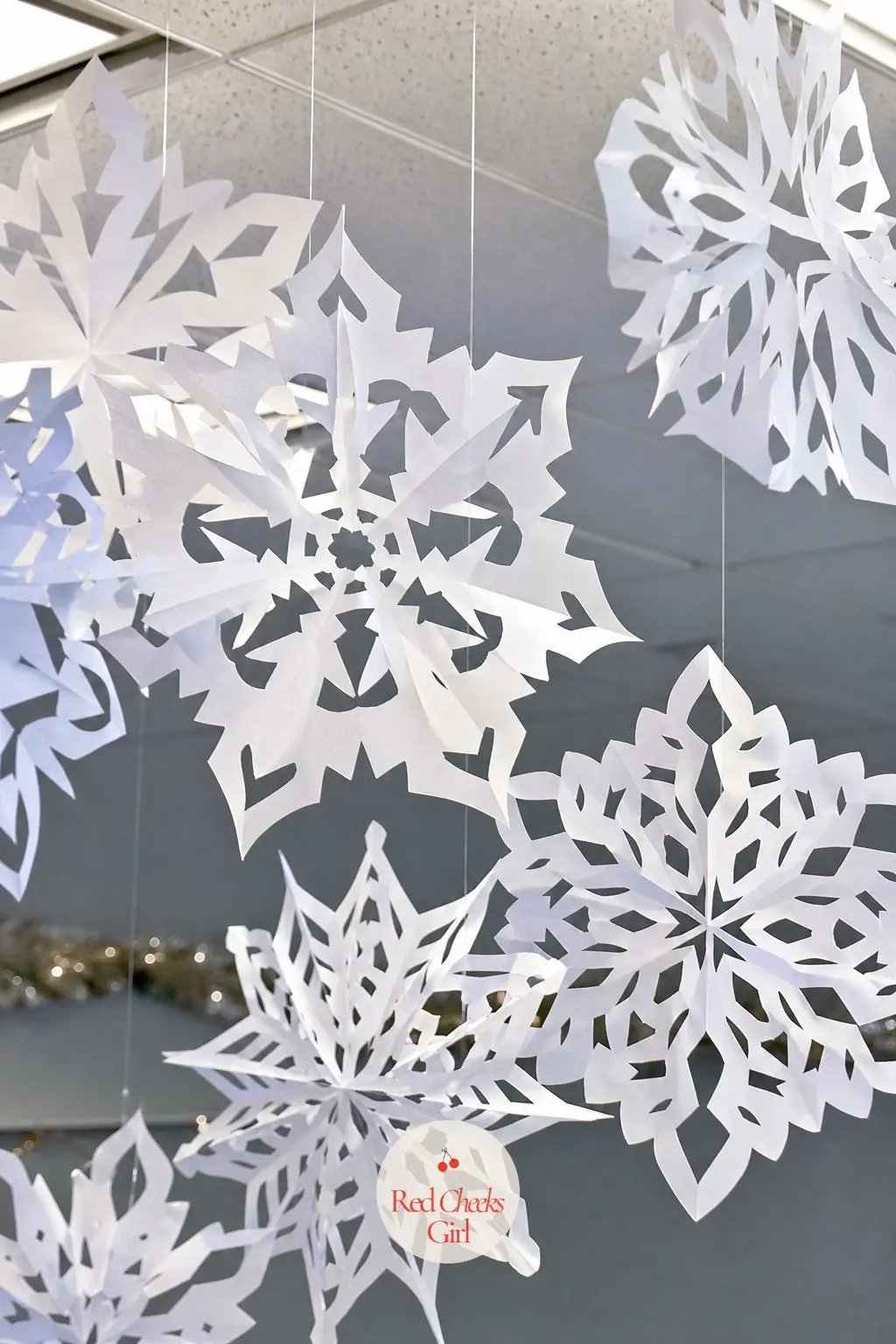 A Row of Oversized Paper Snowflakes Suspended at Different Heights From the Ceiling Grid — Office ceiling grids are built for exactly this kind of hanging
