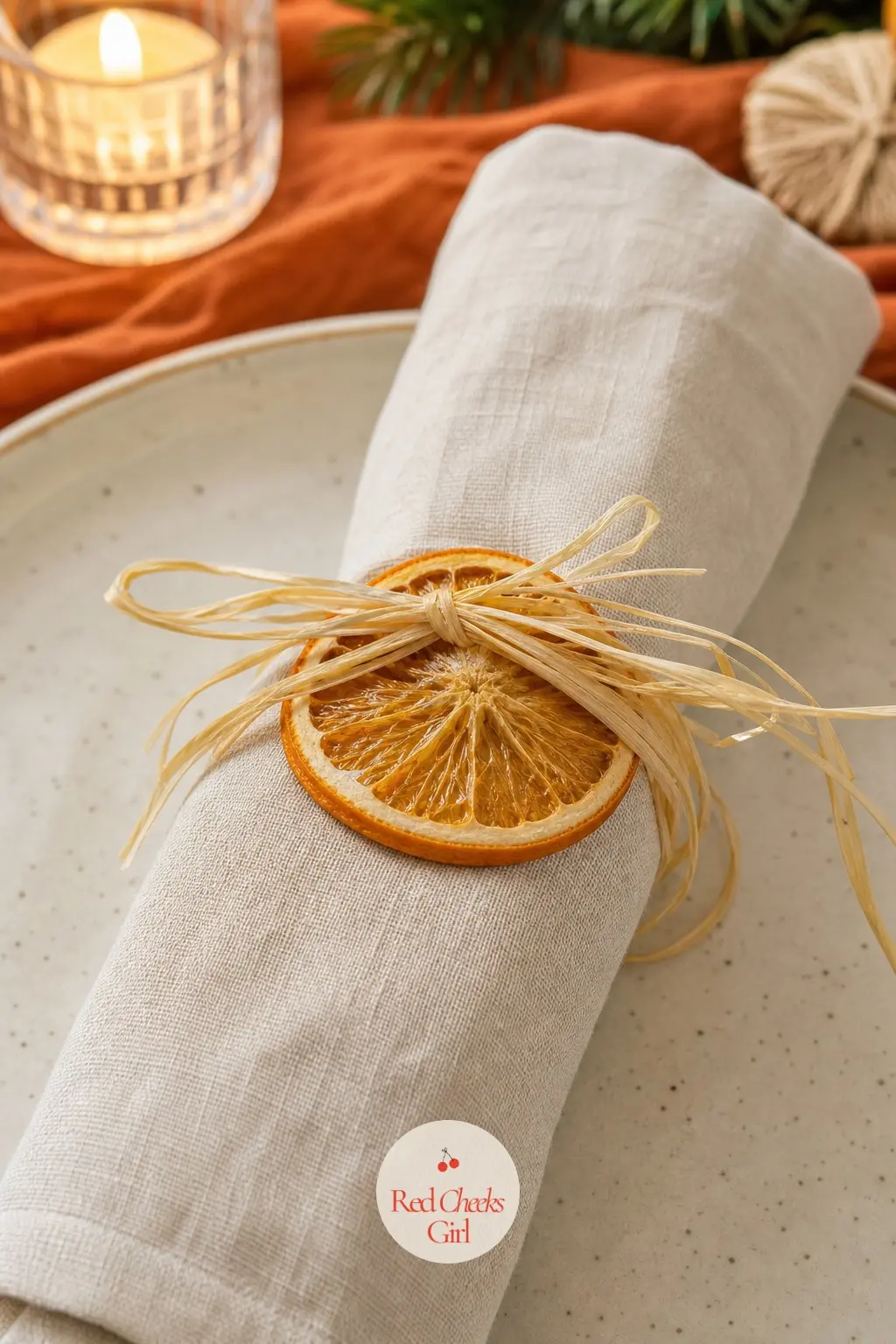 The Place Setting, Tied with Raffia and a Dried Orange Wheel — Each napkin in warm cream linen gets rolled and tied with natural raffia, with a single dried