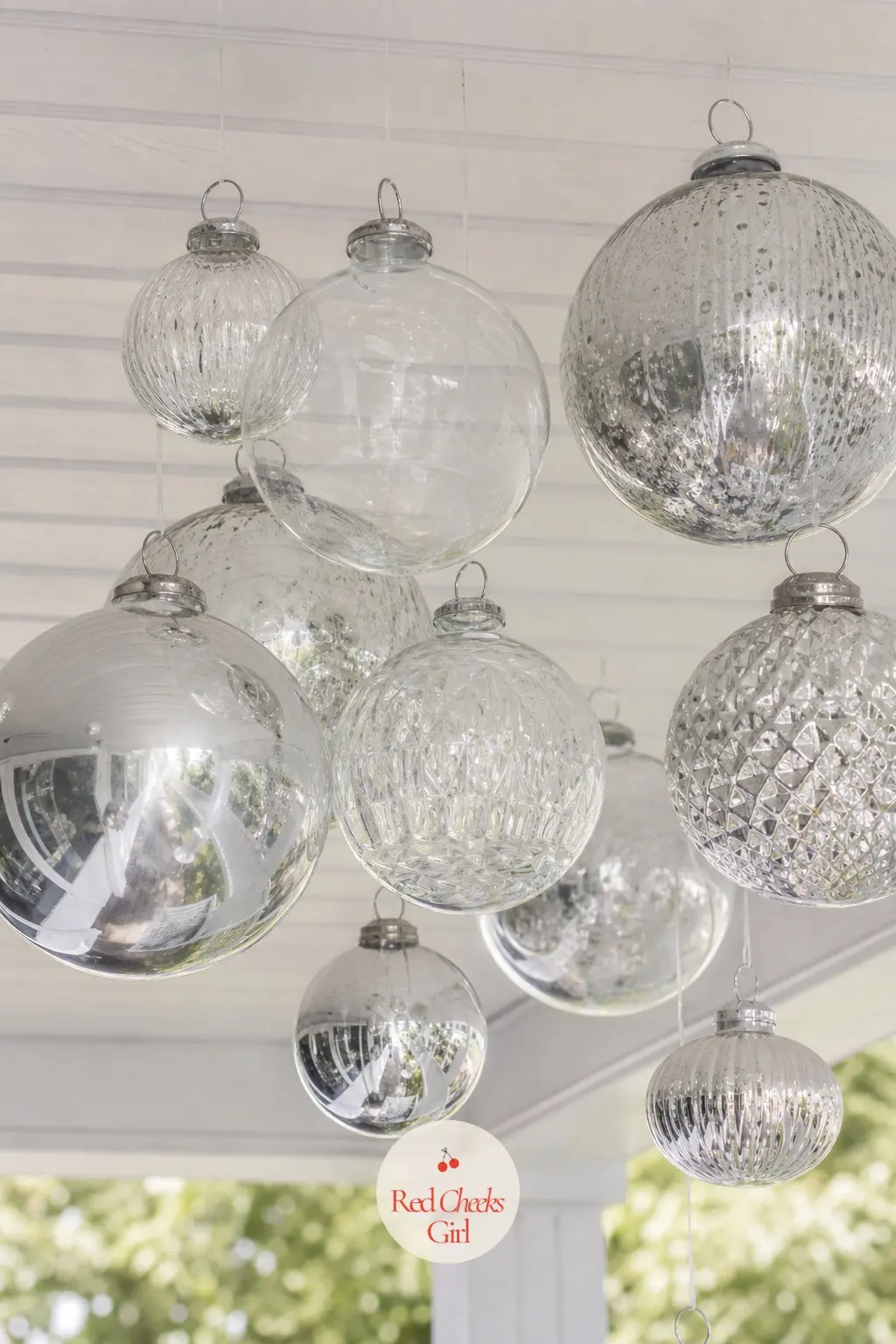 A Porch Ceiling Hung with a Cluster of Oversized Glass Ornaments — Large silver and clear glass balls hang at staggered heights from the porch ceiling on clear