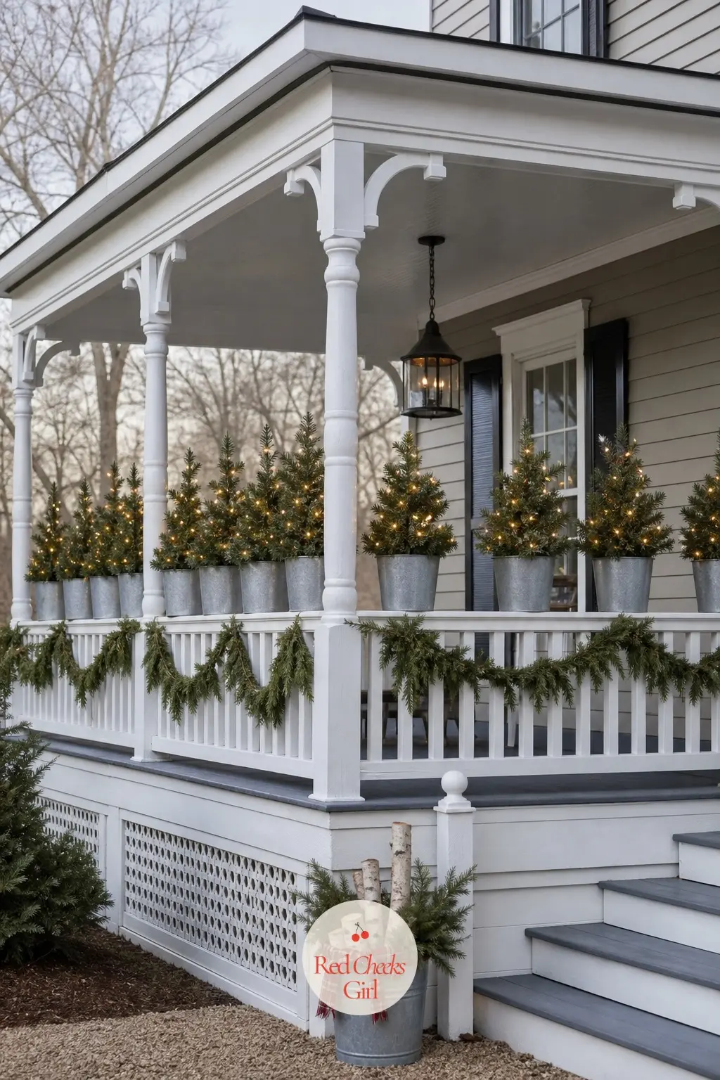 A Porch Railing Lined with Small Lit Trees in Galvanized Buckets — Pre-lit tabletop trees set in galvanized buckets along the top of the railing create a