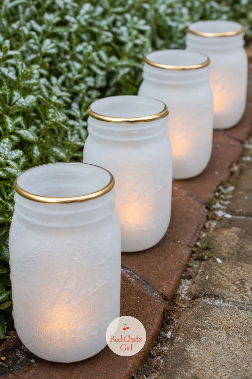 A Row of Luminaries Made from Painted Mason Jars — Mason jars painted frosted white with a thin gold rim at the lip hold battery tealights and line the edge of