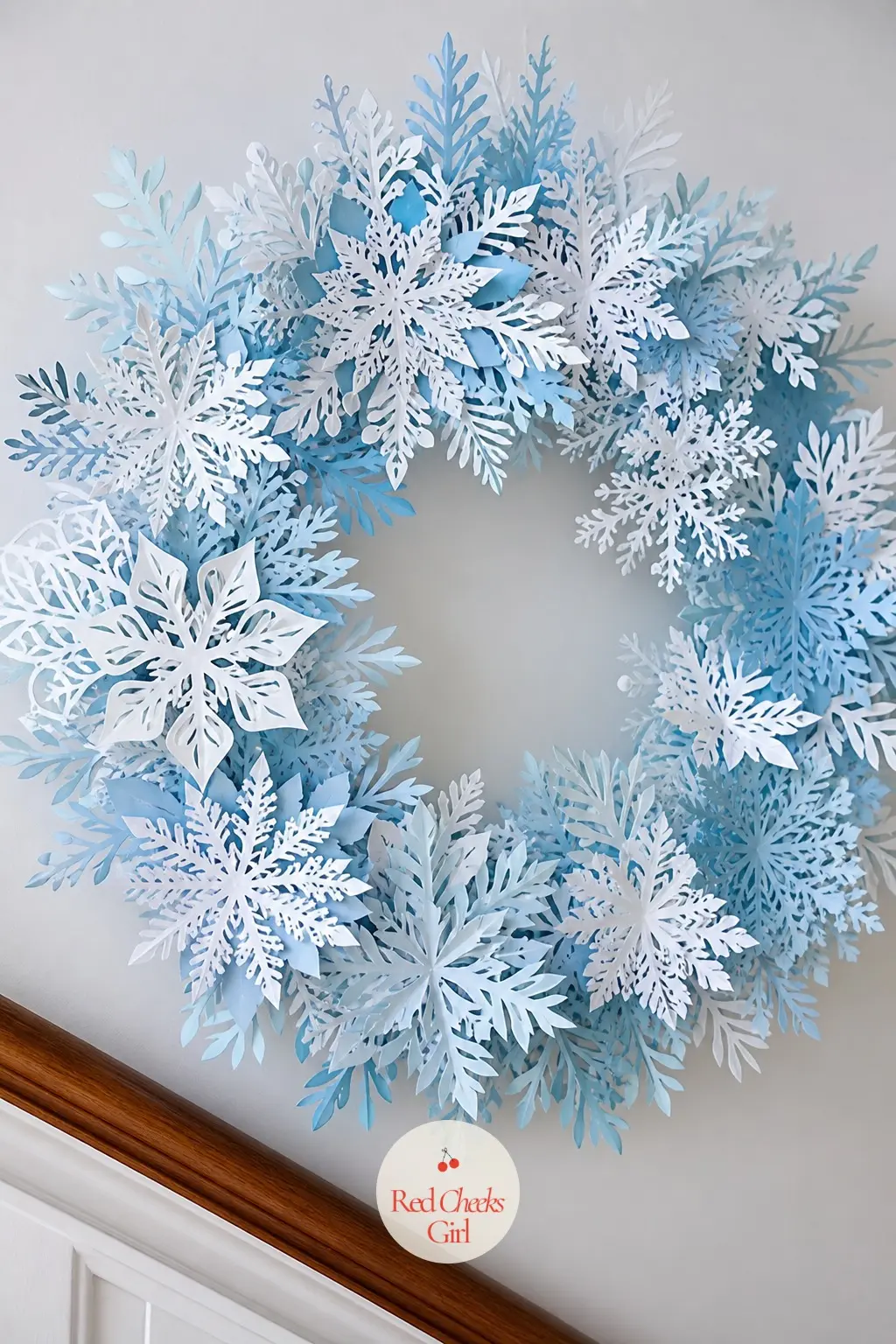 The Frost Blue and White Paper Snowflake Wreath for the Stair Landing — Layers of hand-cut paper snowflakes, frost blue behind plain white, overlap into a ring
