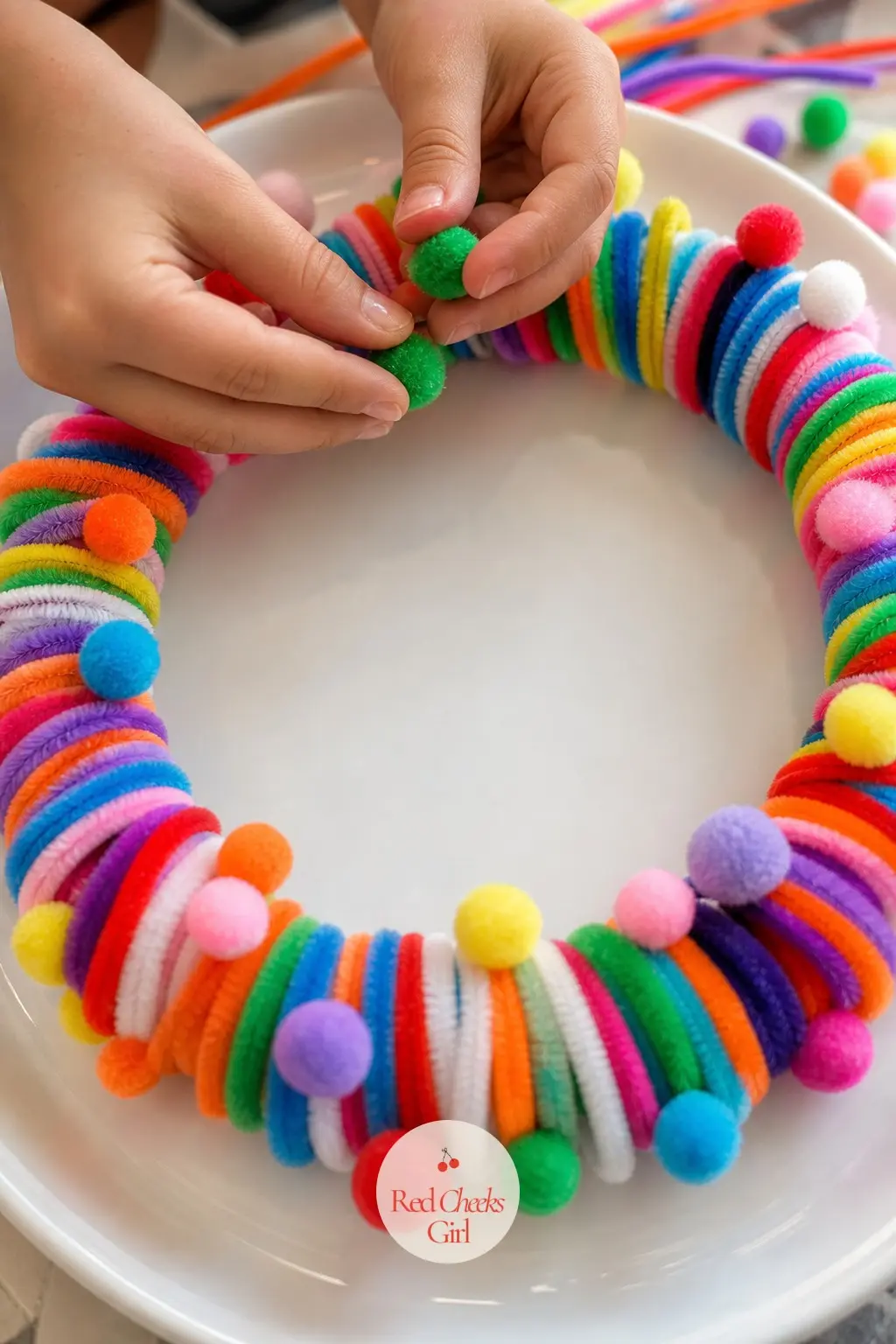 The Rainbow Confetti Pompom Wreath for the Kids Table — Mix every leftover color you own into one coiled loop rather than sorting them, which is the whole