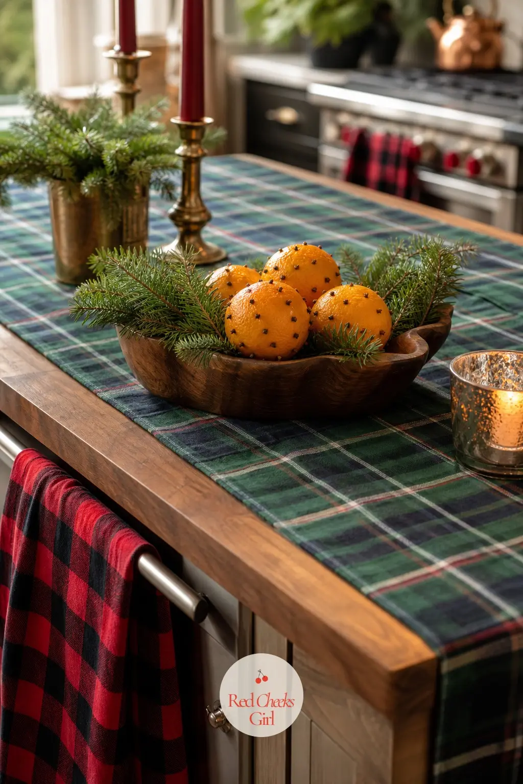 The Kitchen Island, Set for a Snow Day — A tartan runner down the length of the island, a stack of oven mitts in the same pattern, and a bowl of oranges