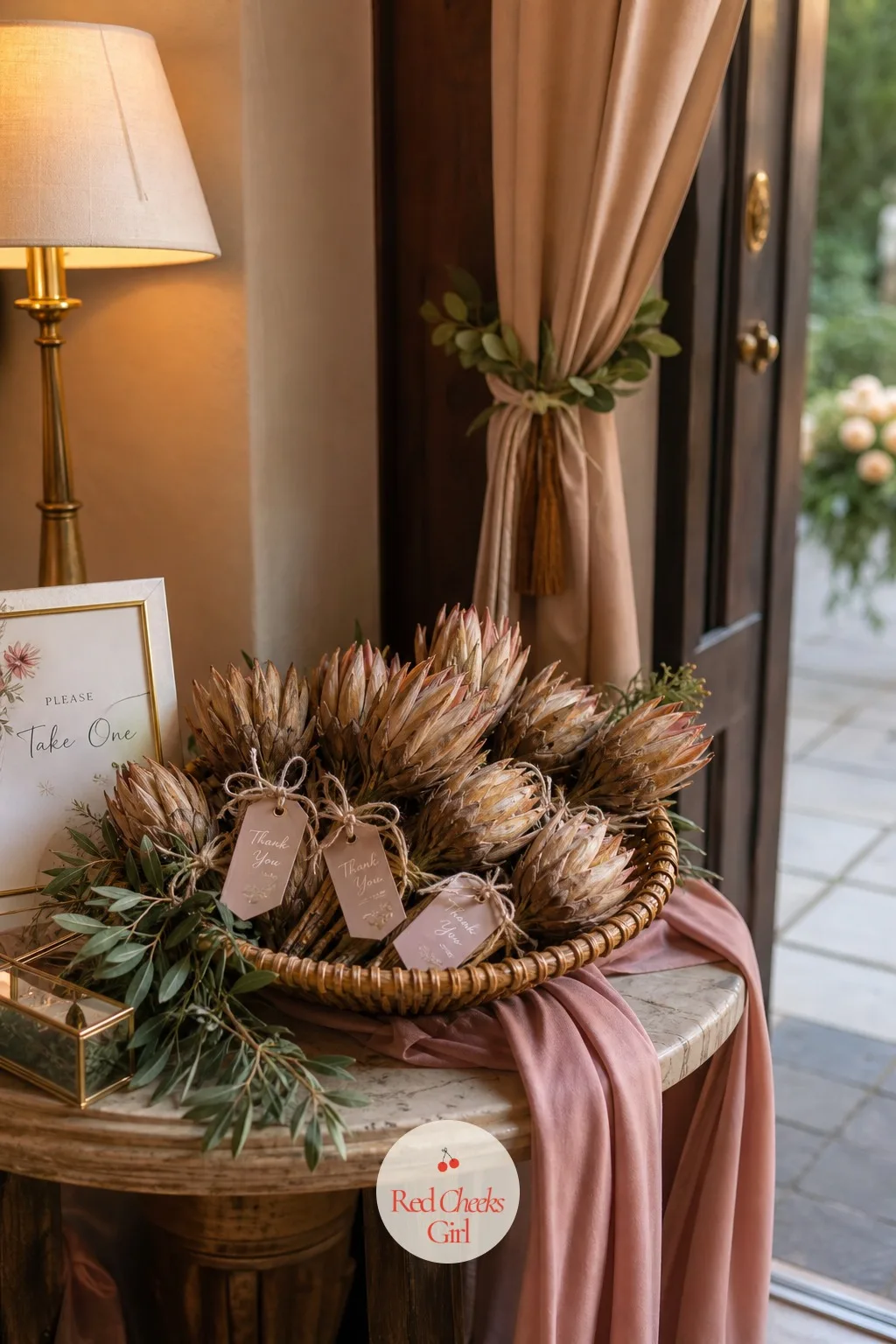 Dried Protea Favors — By the door, a small table holds one dried protea head per guest, tied with twine and a handwritten tag, the cheapest favor on the whole