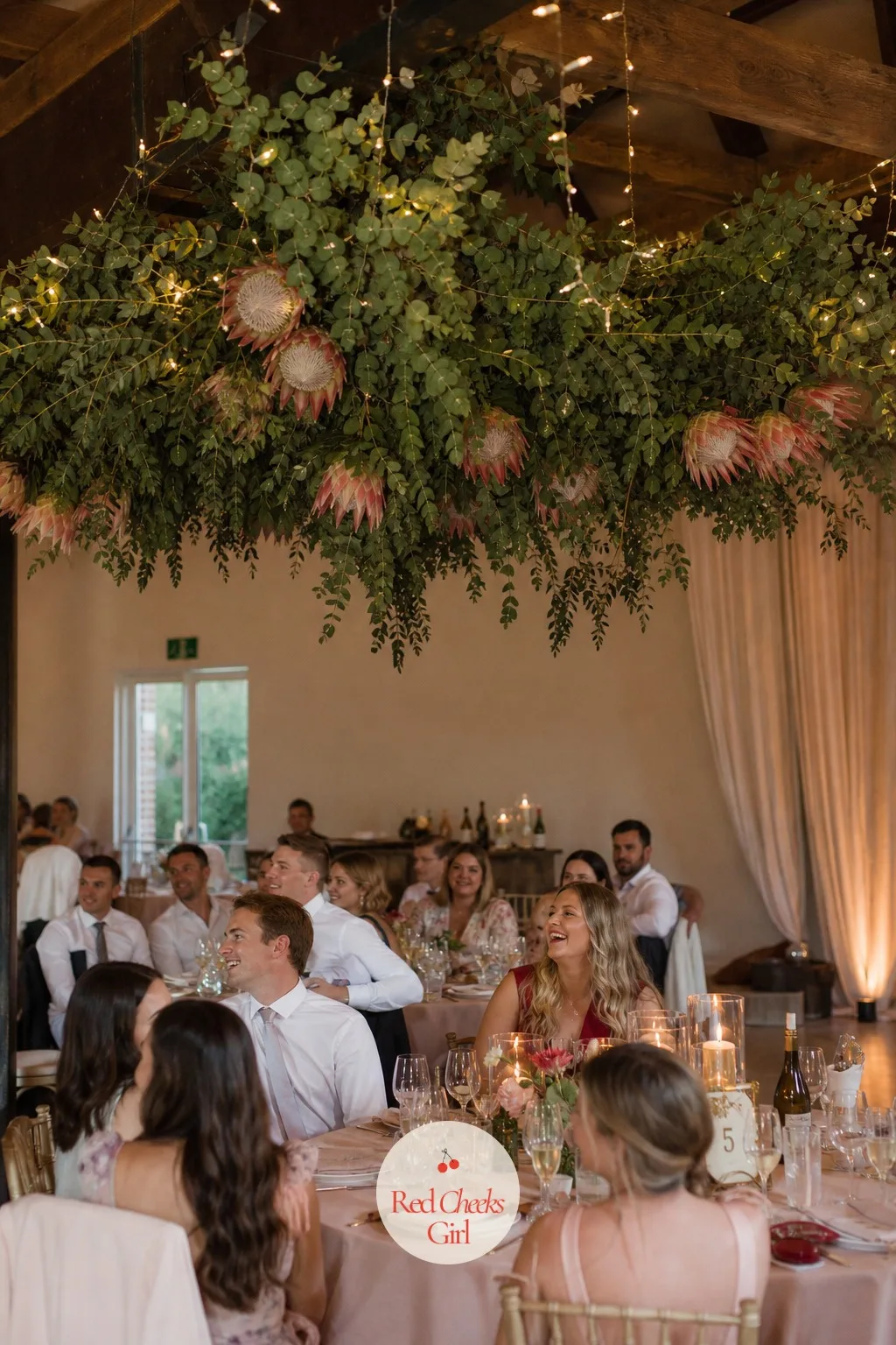 A Protea And Eucalyptus Installation Over The Dance Floor — Above the dance floor, a suspended cluster of eucalyptus and protea hangs from the beams, lit from
