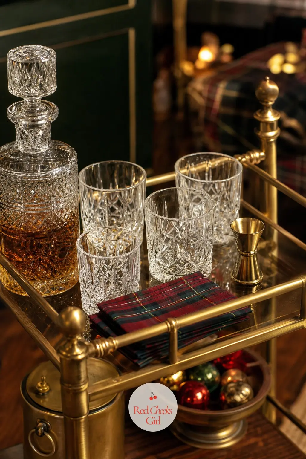 A Bar Cart Poured In Brass And Plaid — A brass bar cart holds a crystal decanter and a set of cut crystal glasses, with tartan cocktail napkins fanned beside a