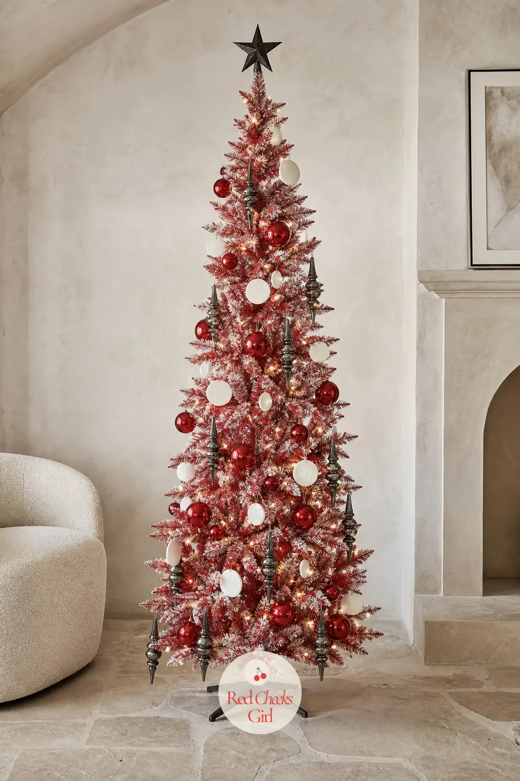A Lacquered Red Tree for the Plaster Room — A sparse, airy artificial tree stands in a pale plaster room with a curved cream chair and a stone floor, its