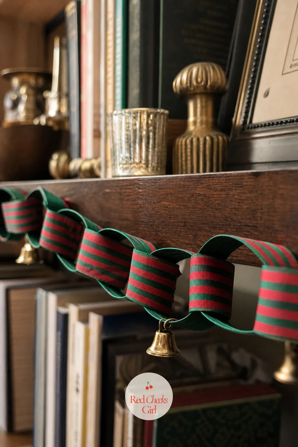 A Ribbon Chain in Red and Green Stripe with Small Brass Bells Along a Bookshelf Edge — A striped ribbon chain reads more playful than the velvet loops