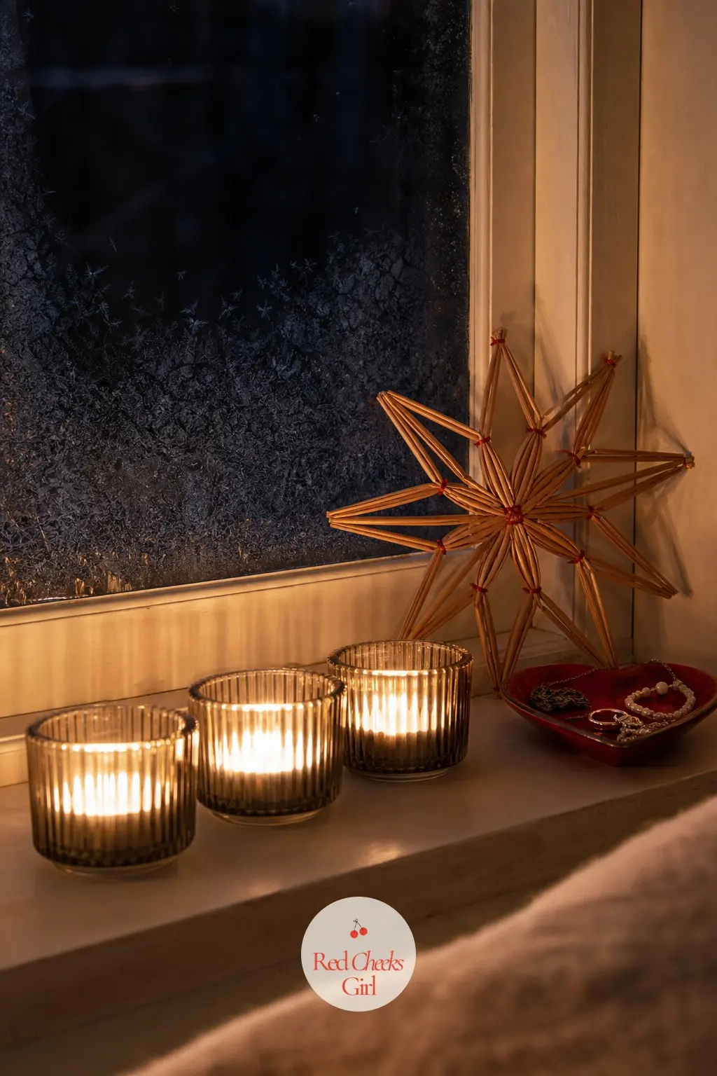 The Bedroom Windowsill, Lit for Reading in Bed — A row of three candles on the bedroom windowsill, one straw star propped against the glass so it catches both