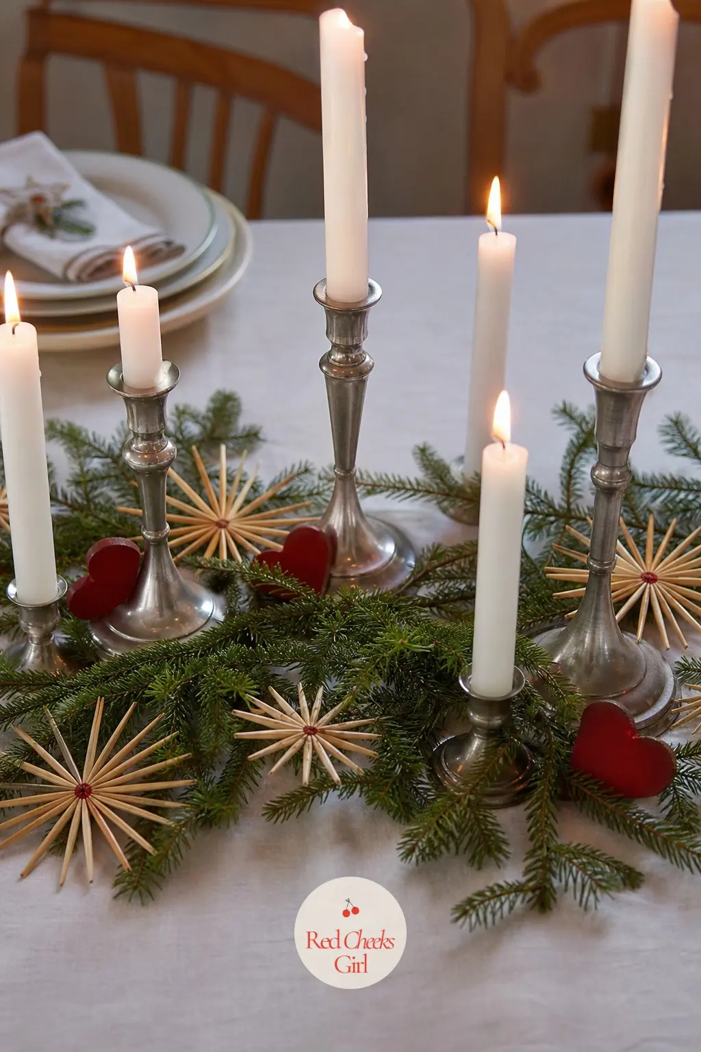 The Table's Centre, Kept to Candles and Straw — No tower of baubles here, just a low runner of greenery with straw stars laid flat among a row of tapers at
