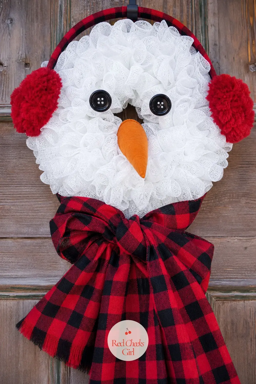 The Plaid Flannel Scarf and Earmuffs Snowman Wreath — A strip of red and black buffalo plaid flannel knotted at the neck turns the plain white body into