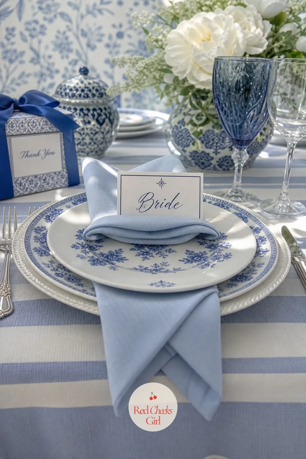 Blue and White Napkin Folds and Place Cards — At each stacked plate, a folded napkin sits with a small hand-written place card tucked into the fold, close