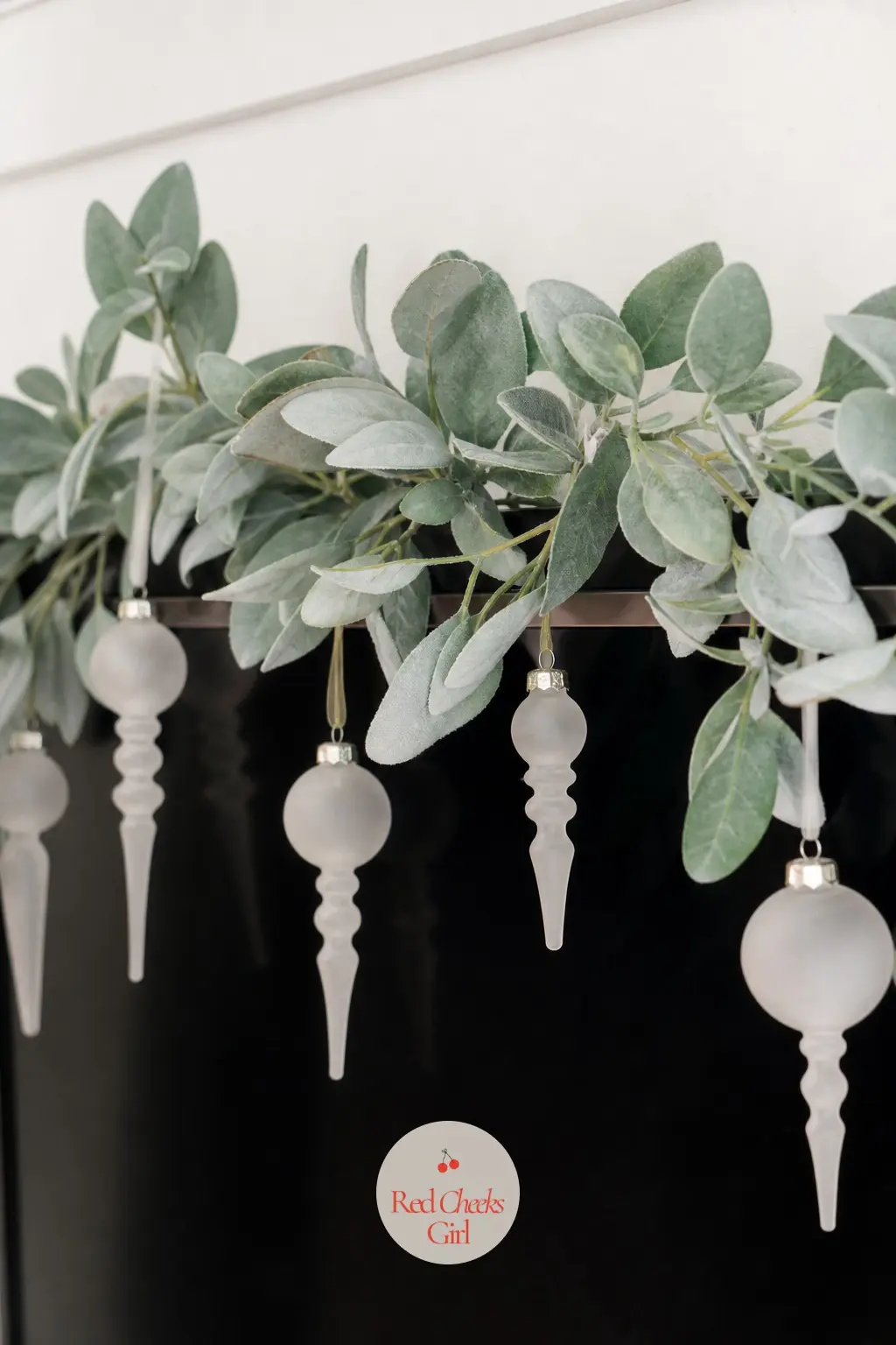 A Garland of Preserved Eucalyptus and Frosted Glass Finials Looped Along the Top Edge — A slim preserved eucalyptus garland loops in one soft curve along the