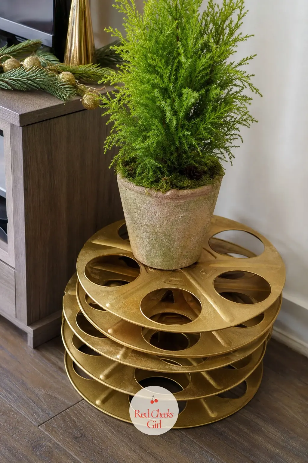 A Stack of Vintage Film Reels Painted Gold Topped With a Potted Cypress — Three old film reels, the metal kind rather than plastic, get a coat of gold spray