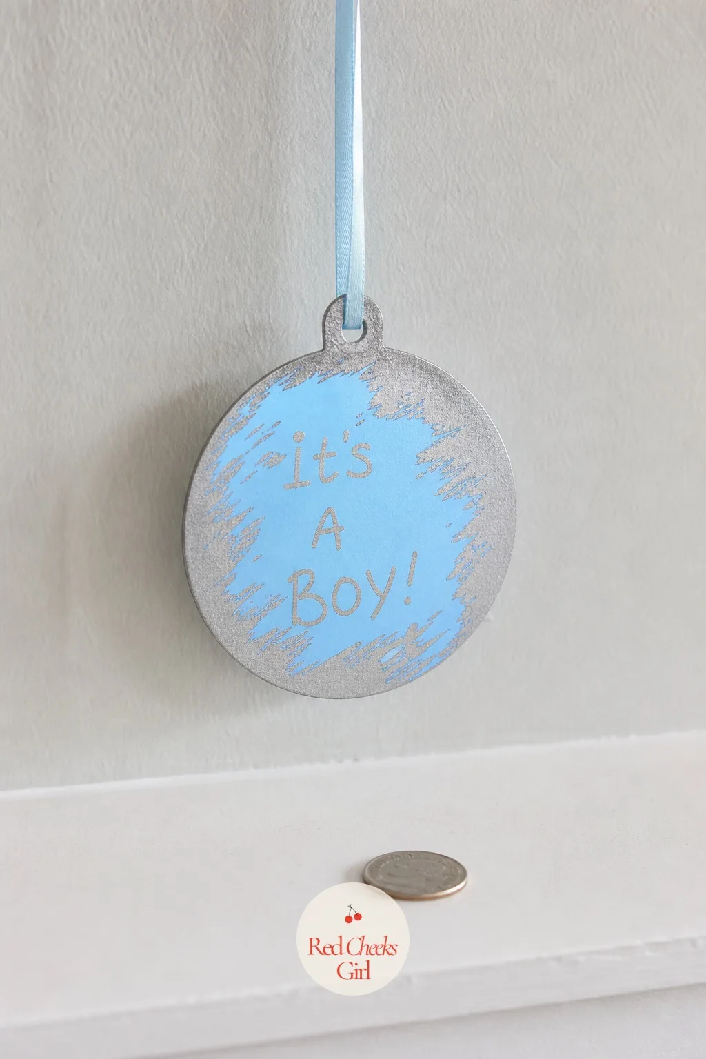 Scratch-Off Ornament Reveal — A plain round ornament hangs from a ribbon looking like any other bauble, until a coin scrapes away the top coat and a painted
