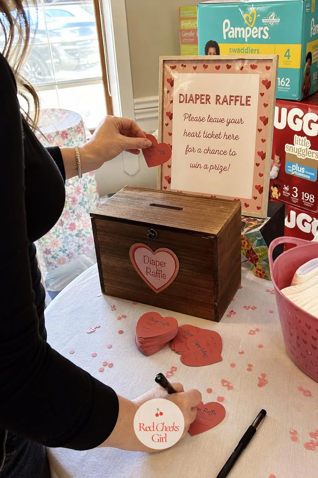 Diaper Raffle Heart Ticket Station — A small wood box with a slot cut in the top, a stack of heart-shaped raffle tickets and a pen beside it, and a sign