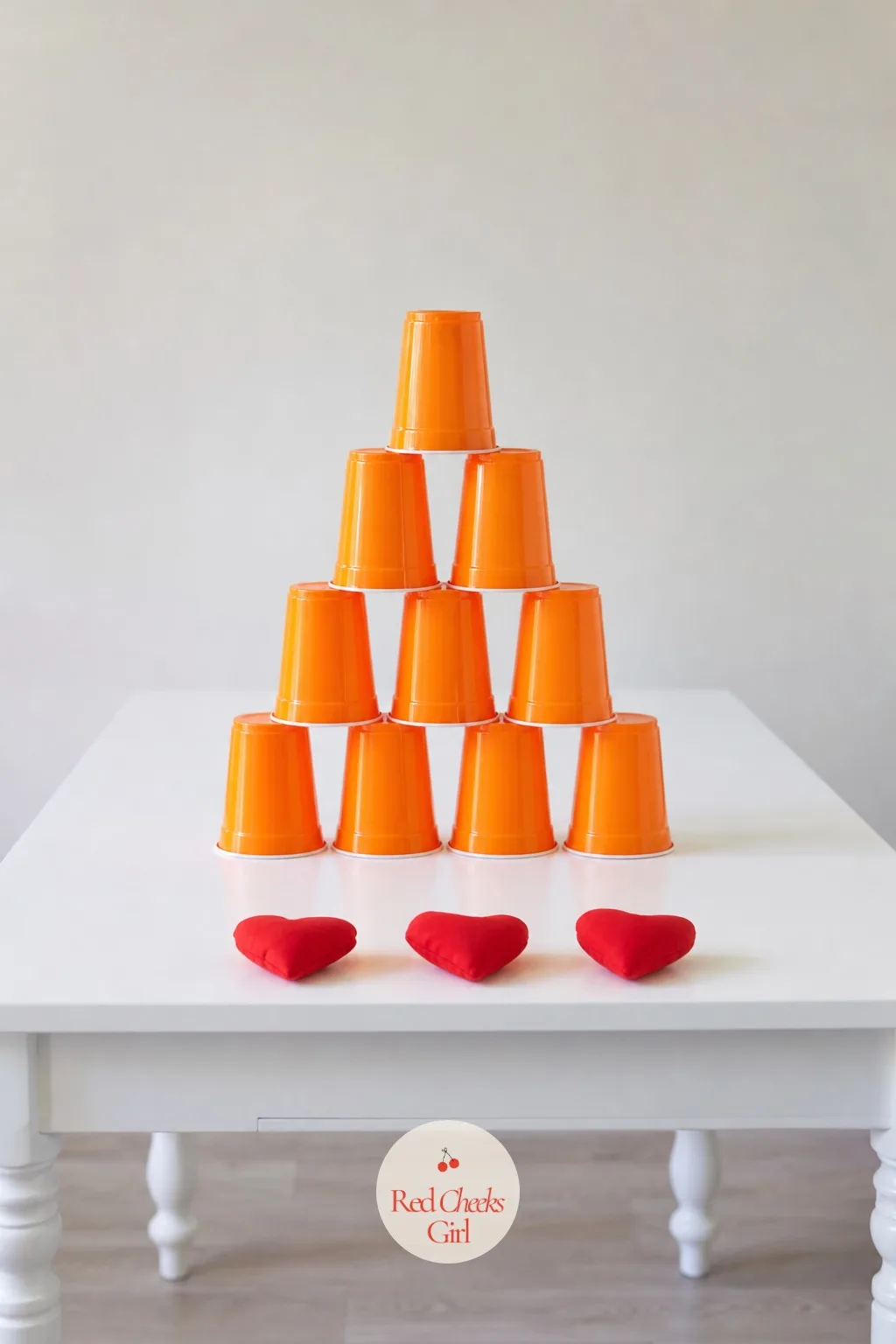 Heart Beanbag Cup Castle Knockdown — Stack a pyramid of plastic cups on a table edge, hand each player three small heart-shaped beanbags, and let them throw