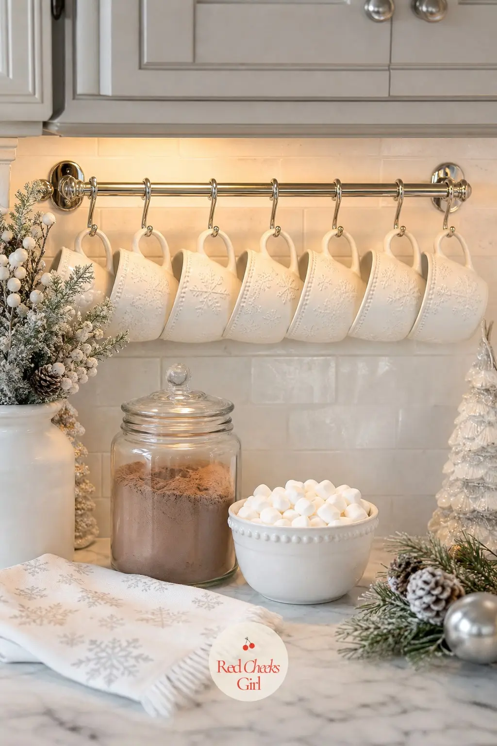 The Cocoa Mugs, Hung on a Silver Rack — Six white ceramic mugs hang from a silver rack above the counter, a jar of cocoa mix and a small bowl of mini