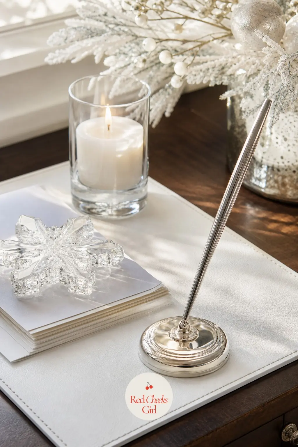 The Desk Vignette, Set With a Silver Pen — A plain white blotter sits under a silver pen holder, a small glass snowflake paperweight keeping a stack of