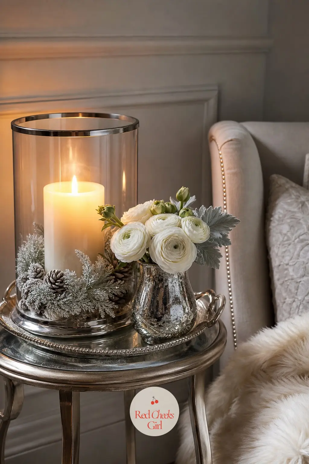 The Side Table, Lit With a Single Candle — A side table carries one glass hurricane, three white pillar candles inside it, and a small vase of white ranunculus